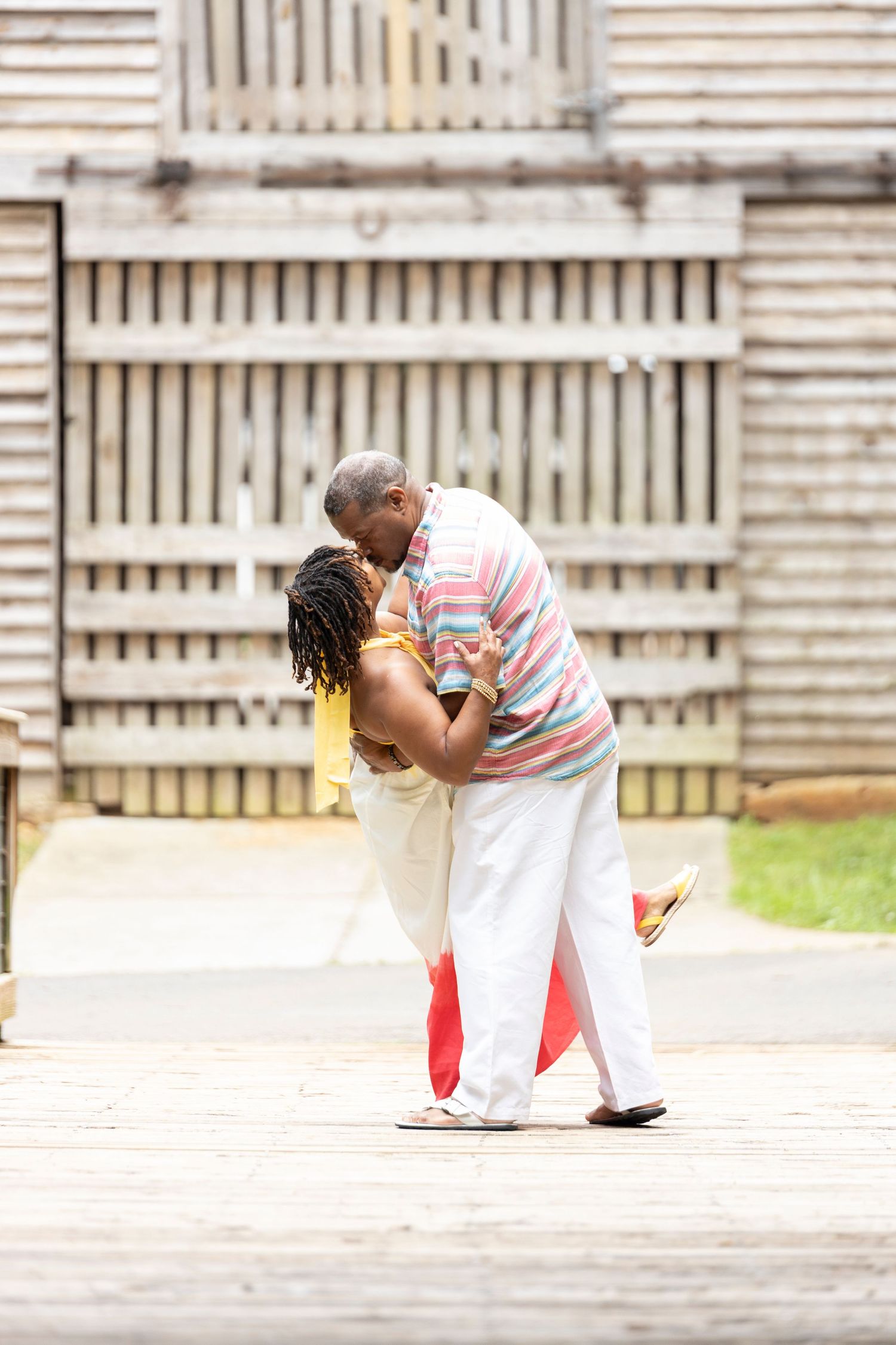 A person in red and white stripes bends down to embrace a small dog on a paved surface.
