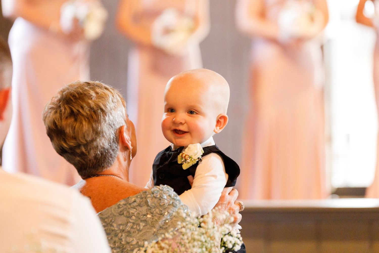 A small baby in formal attire being held up during a wedding ceremony.