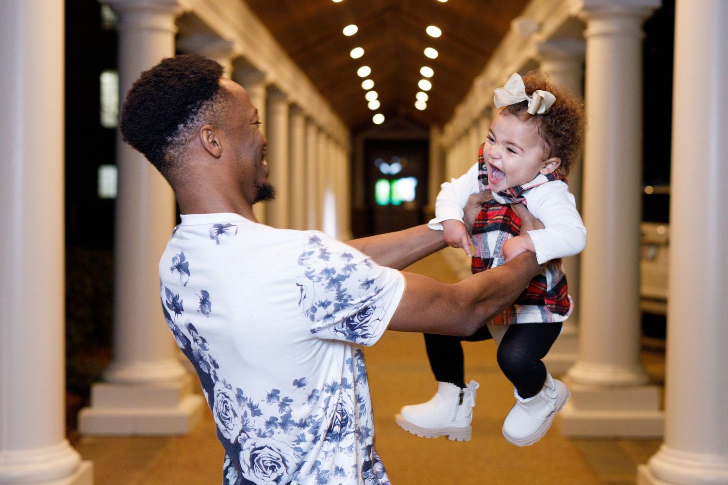 Two people practice boxing techniques in an elegant hallway with white columns and overhead lighting.