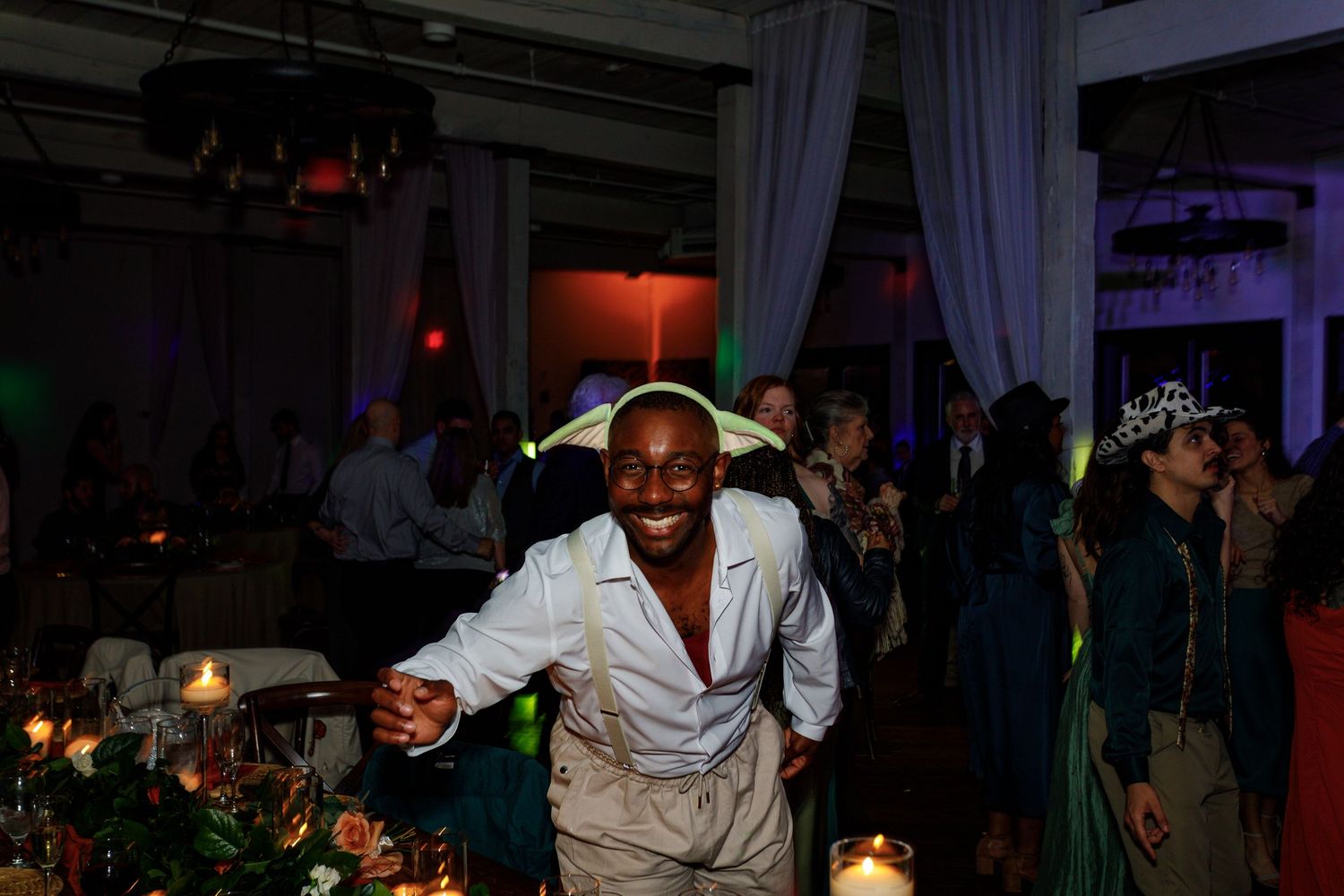 A joyful wedding guest dances at the reception surrounded by candlelight and ambient lighting.