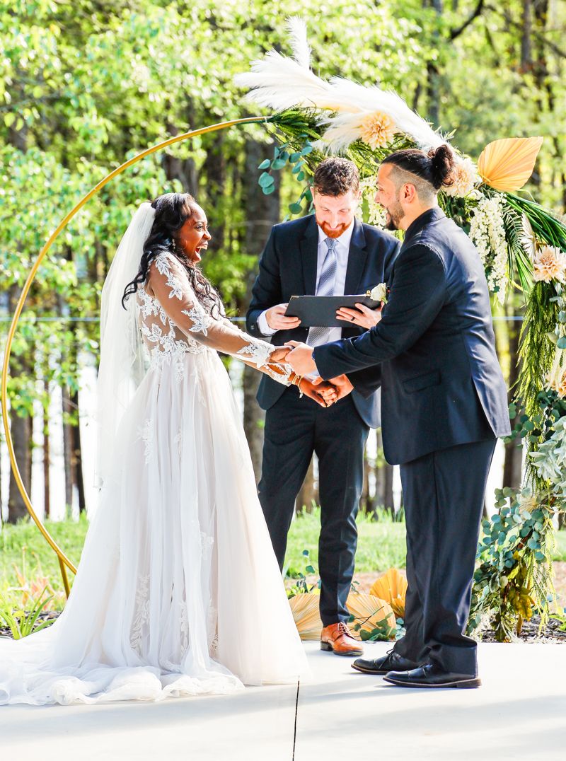 An outdoor wedding ceremony under a floral arch with the couple exchanging vows.