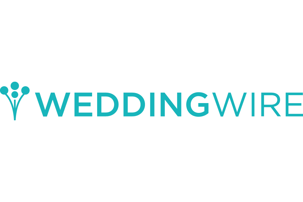 A modern bride and groom kiss while standing in front of a white brick wall with greenery.