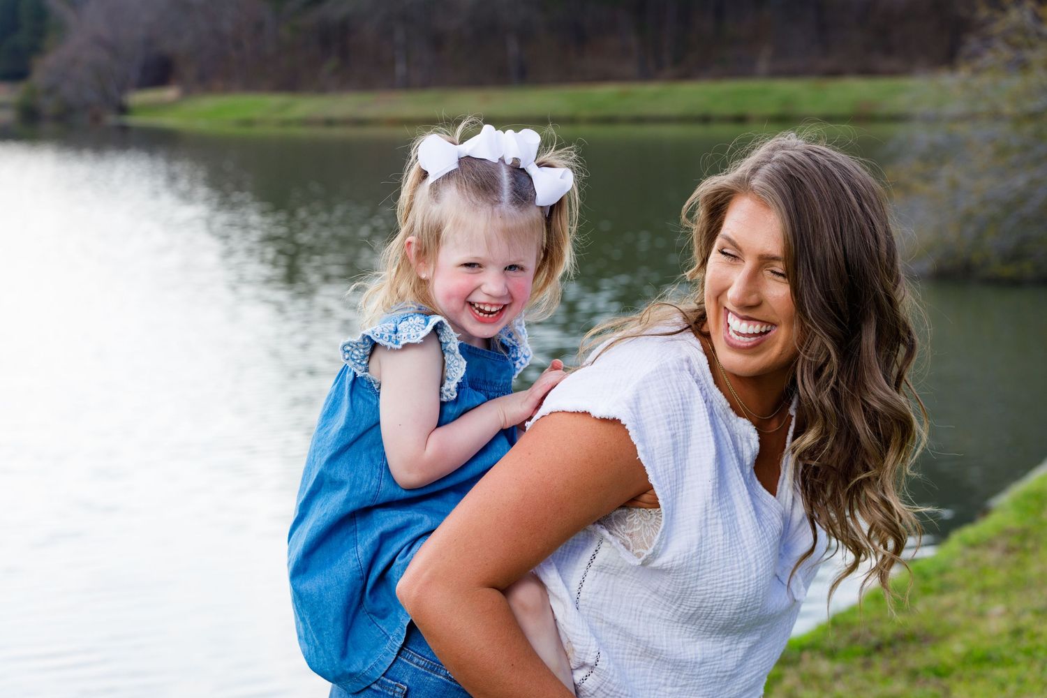 A parent and child in blue clothing share joyful moments together during an outdoor photo session near a lake.