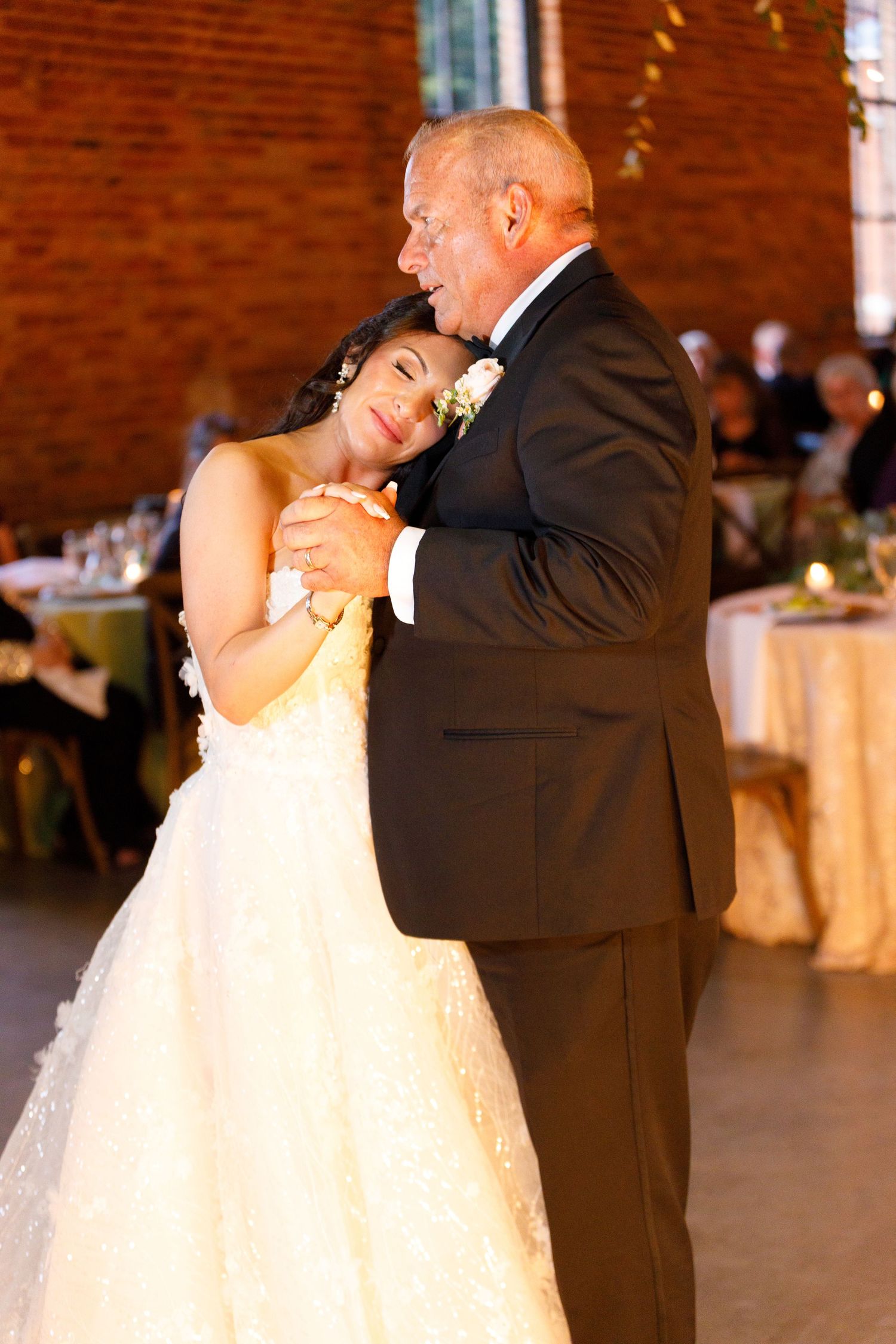 Romantic dance sequence between couple in formal attire inside brick-walled reception venue.