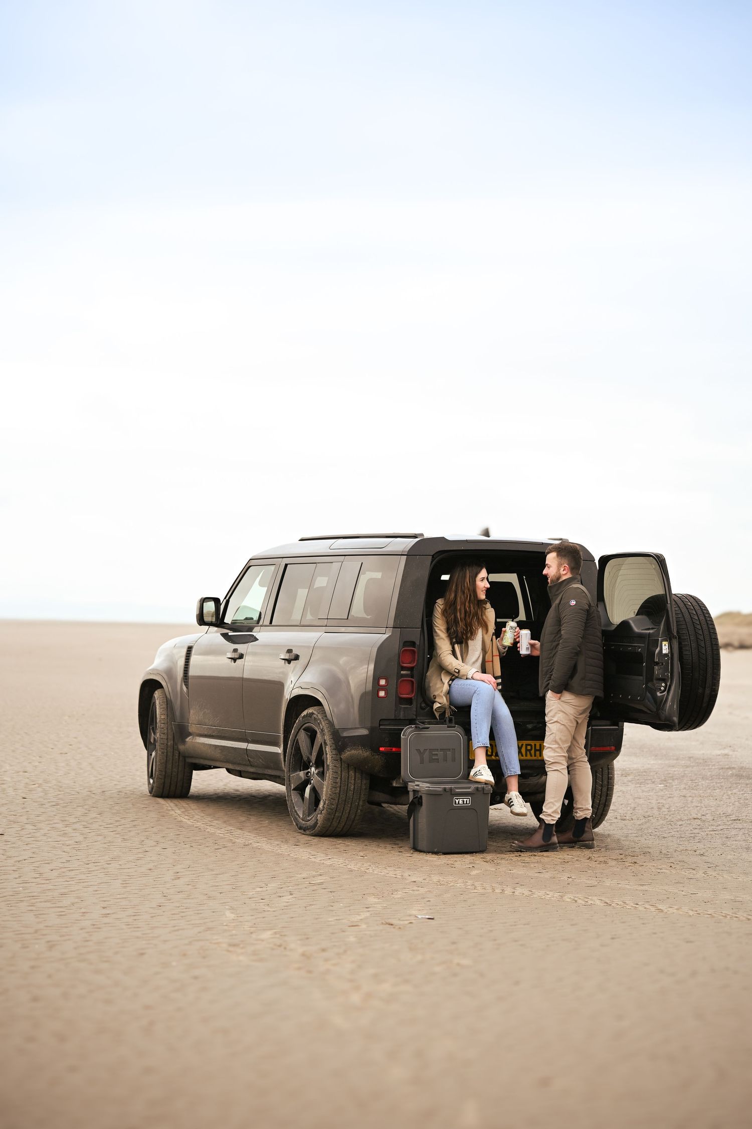 Engagement shoot on the beach in Black Rock Sands, Porthmadog. Couple standing next to their Landrover and Yeti