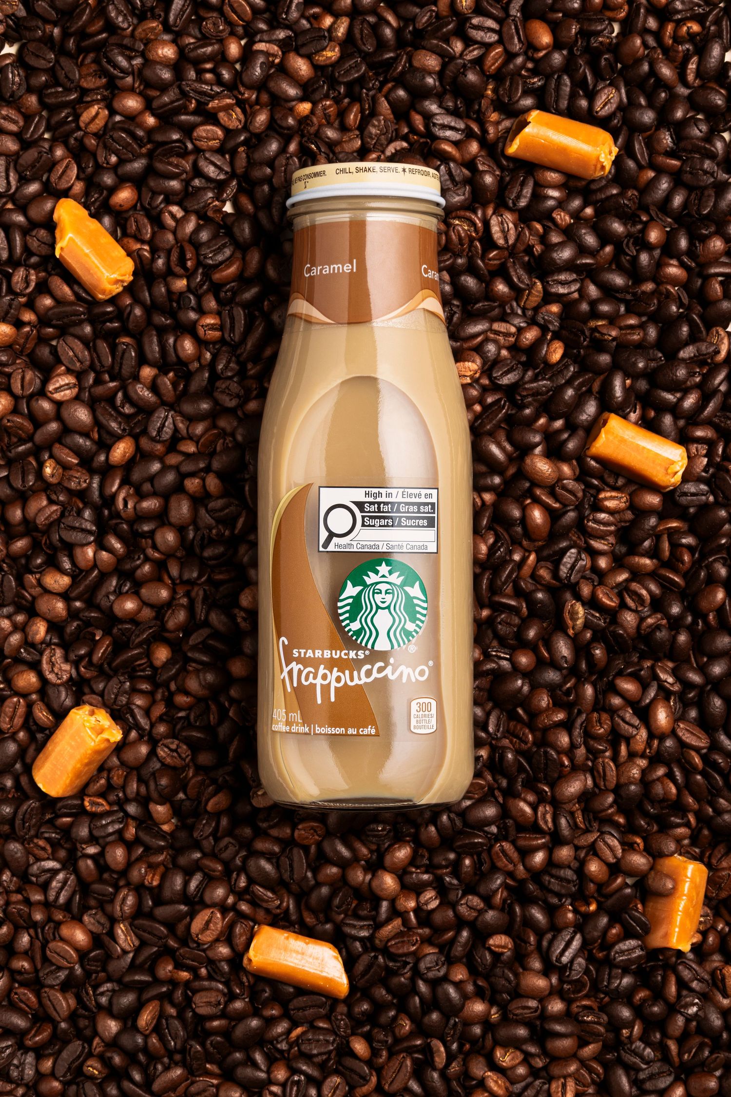 Starbucks Caramel Frappuccino laying on a bed of coffee beans and caramel