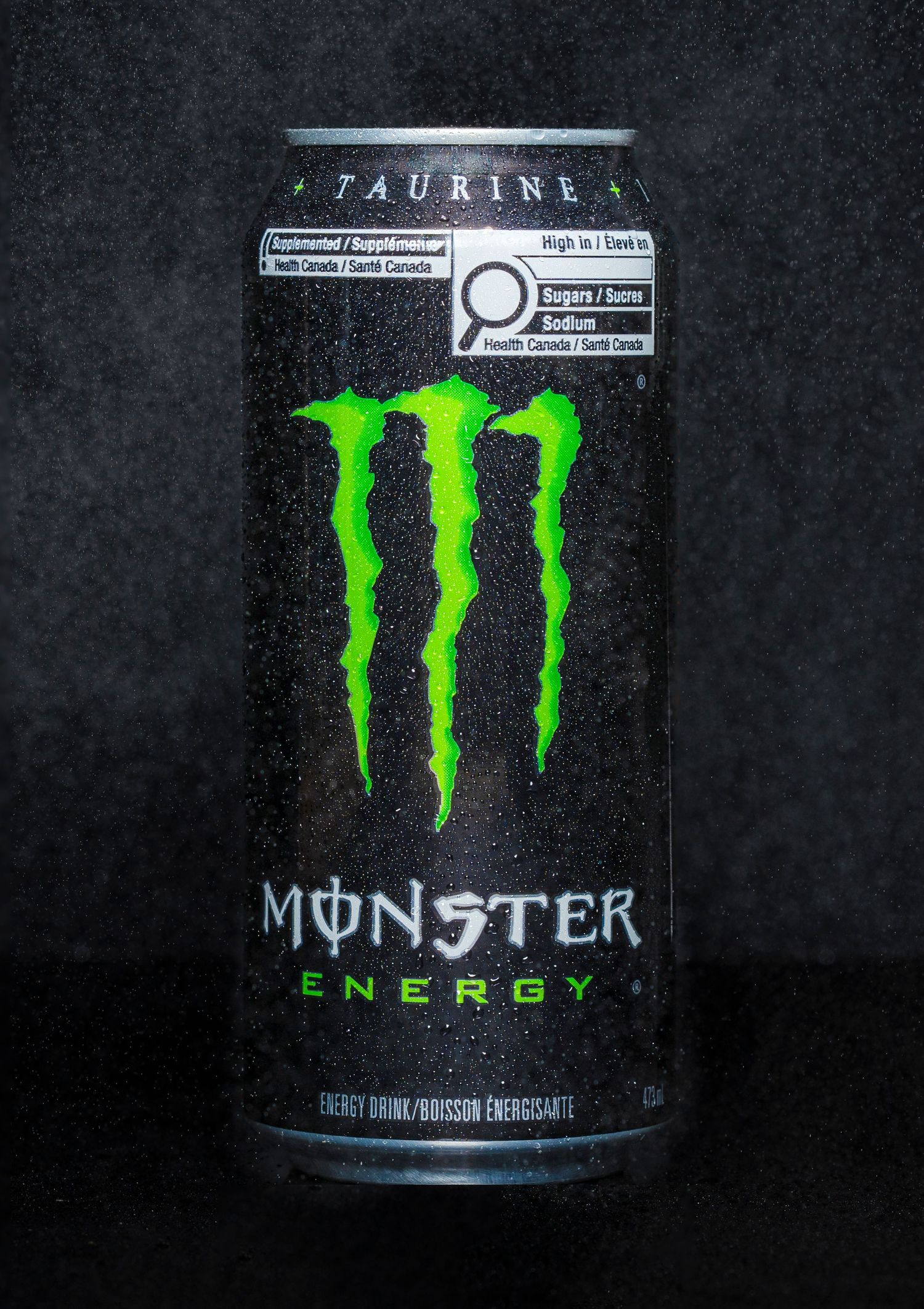 Monster can on a black background water spraying on and behind the can