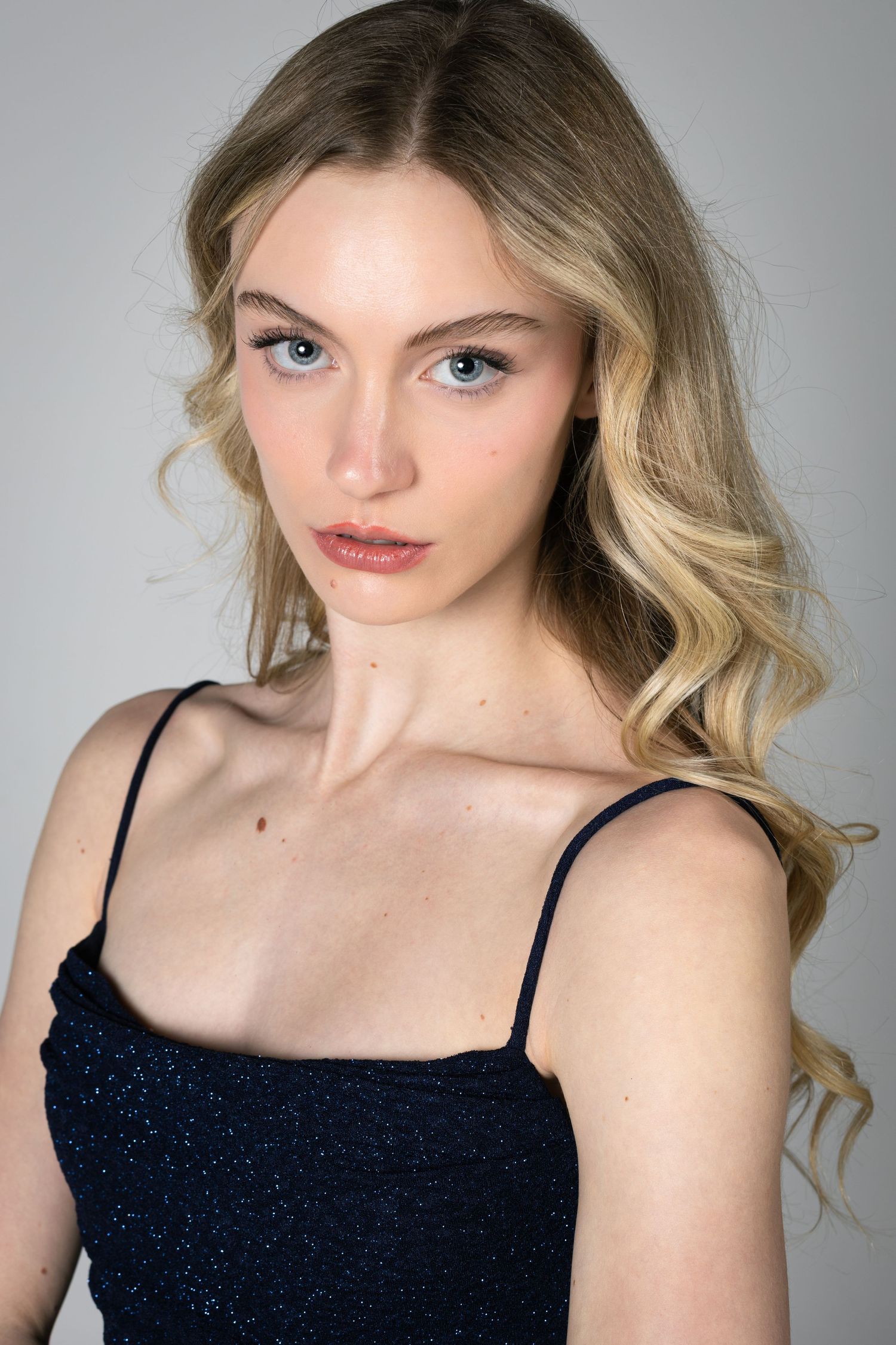 Elegant beauty portrait of blonde model with wavy hair and intense gaze on gray background.