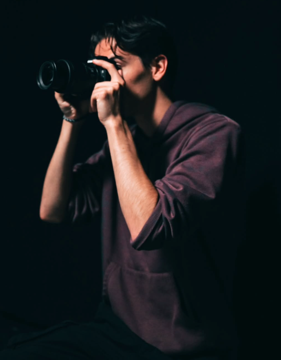Moody portrait of a male photographer holding a camera to his eye in low-key dark lighting.