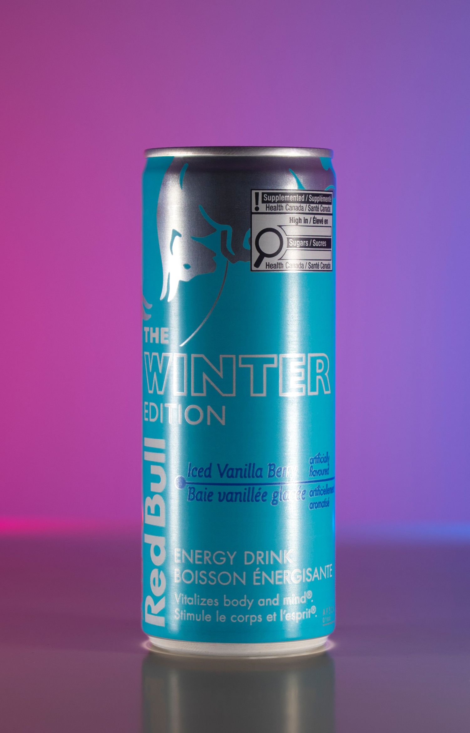 Red Bull Winter Edition can on purple and pink background, energy drink product photography.