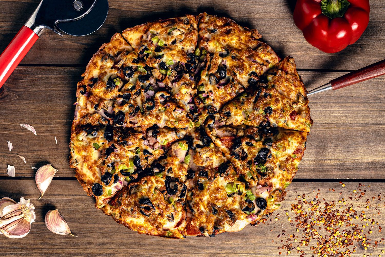 Close-up food photography of sliced loaded pizza with olives, peppers, and cheese on wooden table.