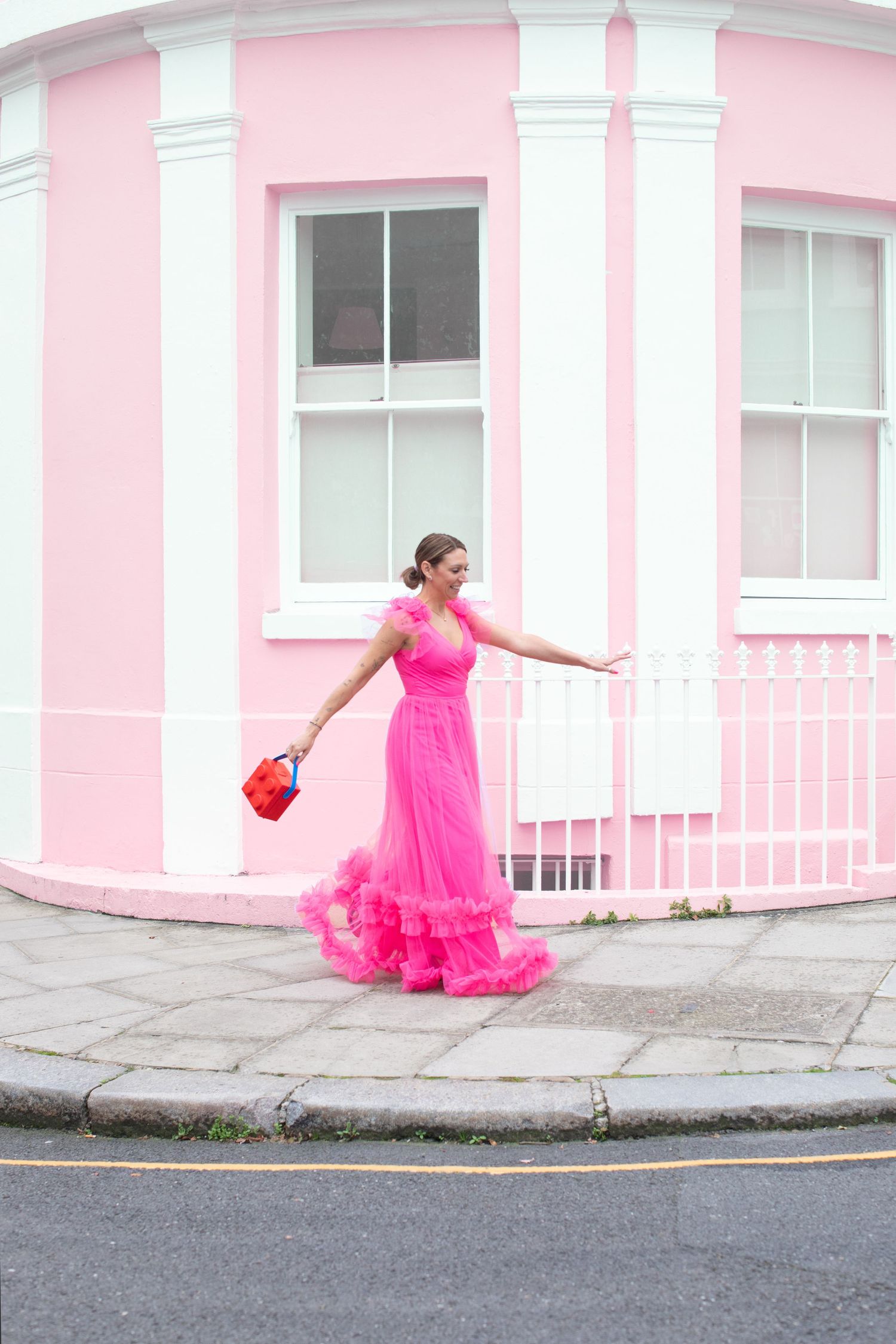 Dancing sequence in a flowing hot pink dress against a pink building exterior.