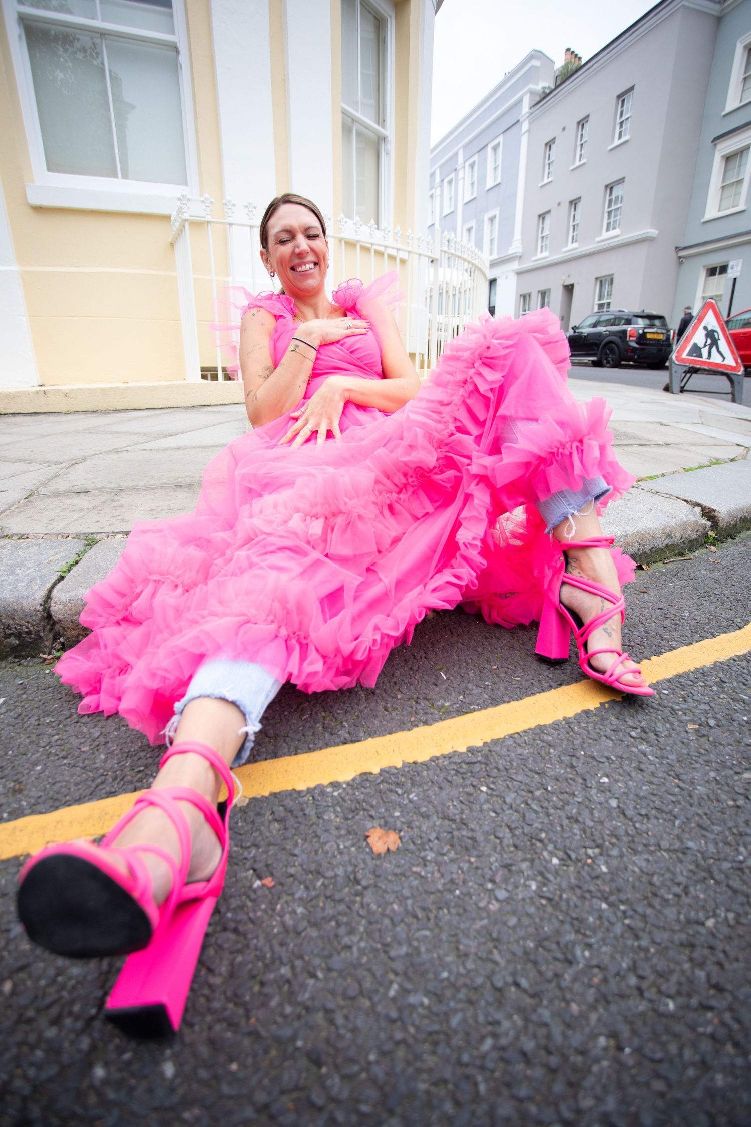 Person lying on street wearing vibrant pink tulle dress and matching boots.