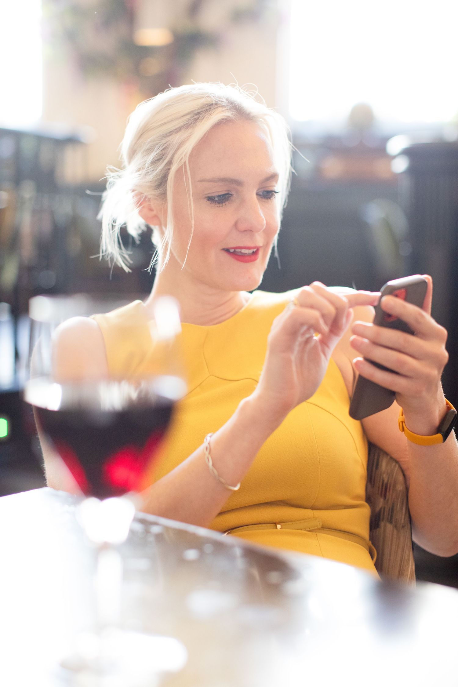 Person in yellow top looking down at mobile phone while sitting at table.