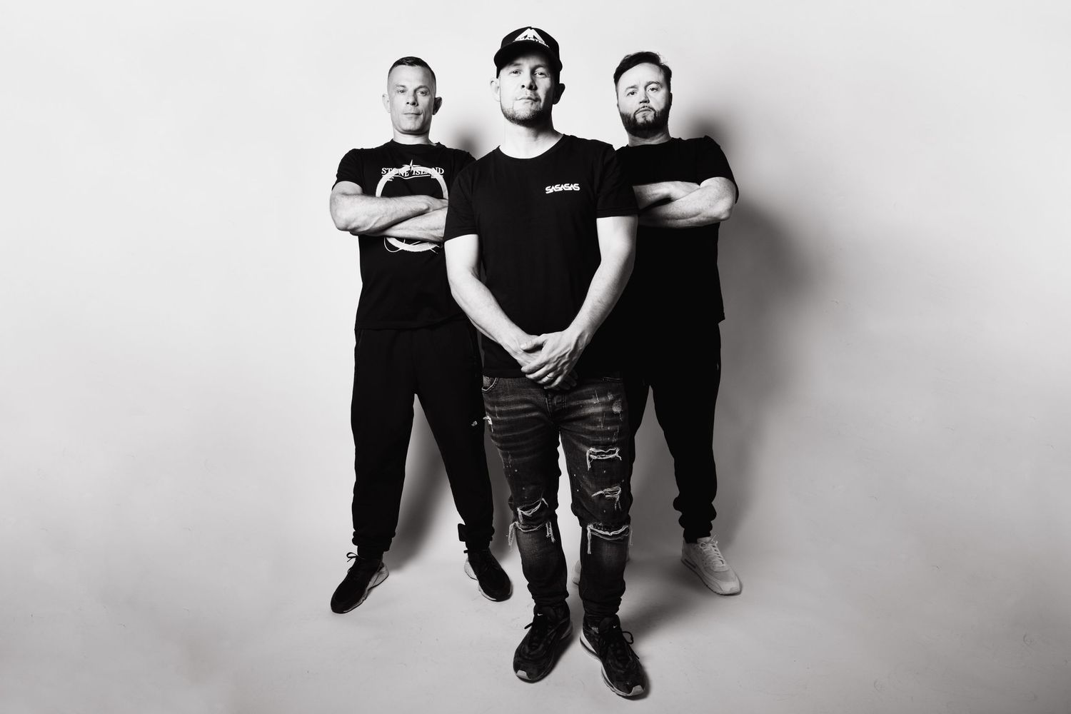 Black and white group photo of three people in matching dark outfits against white backdrop.