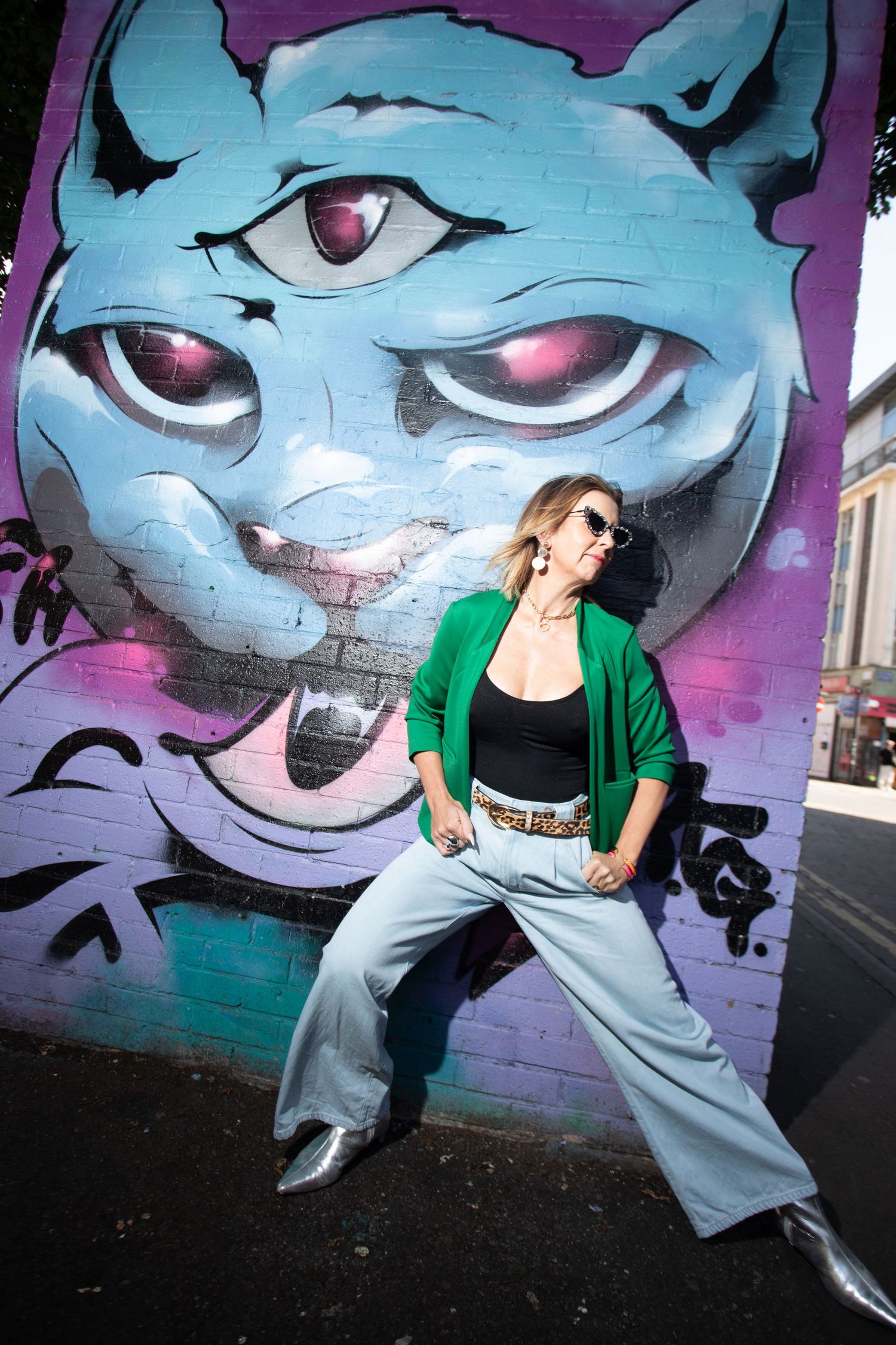 Person in green jacket poses against large blue character street art mural.