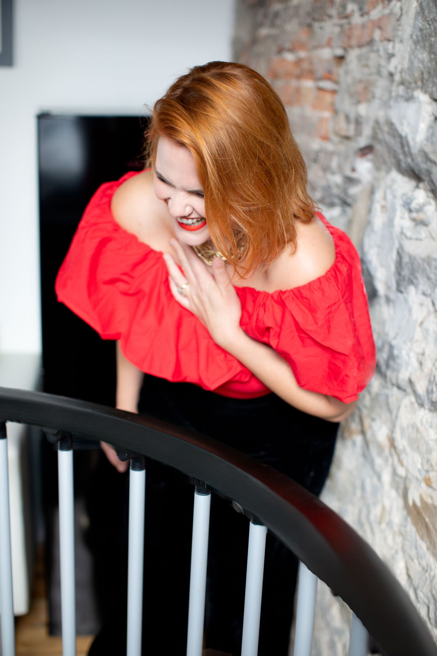 Candid laughing shots in red ruffled top against industrial brick wall and railing.