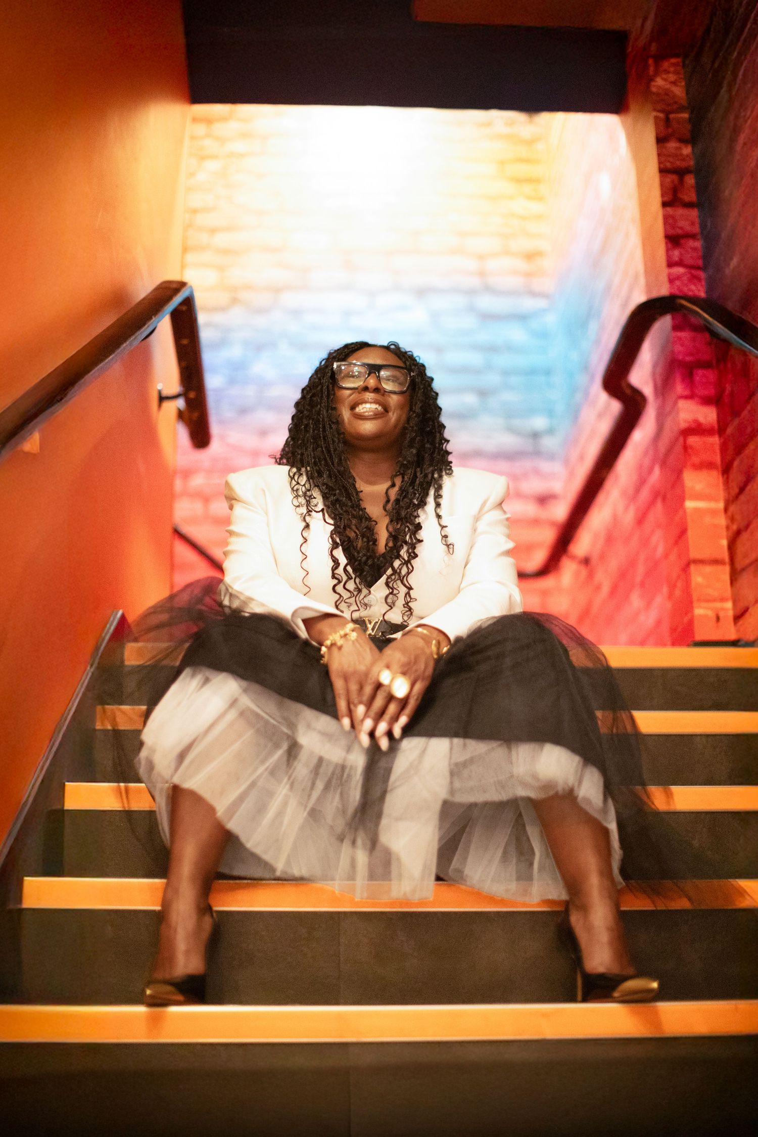 Person in tulle skirt sitting on wooden steps with warm lighting and dramatic shadows.