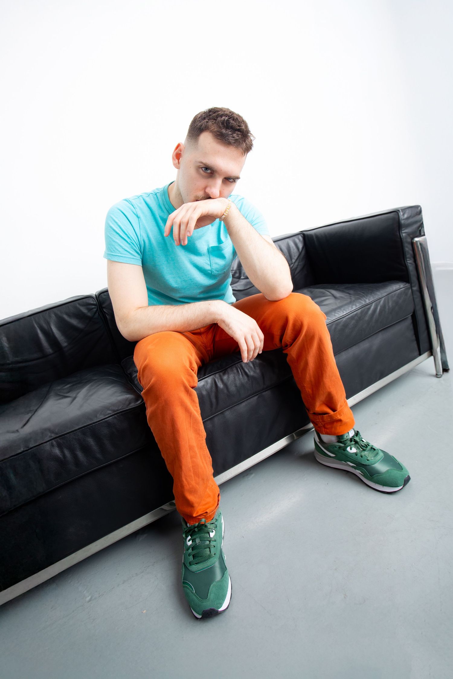 Man in teal shirt and orange pants sitting on black leather sofa.