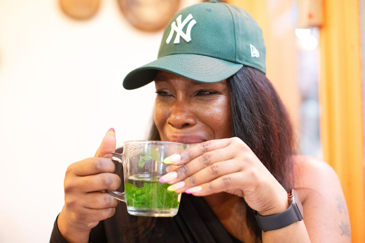 Person in baseball cap holding green drink in sunlit setting.
