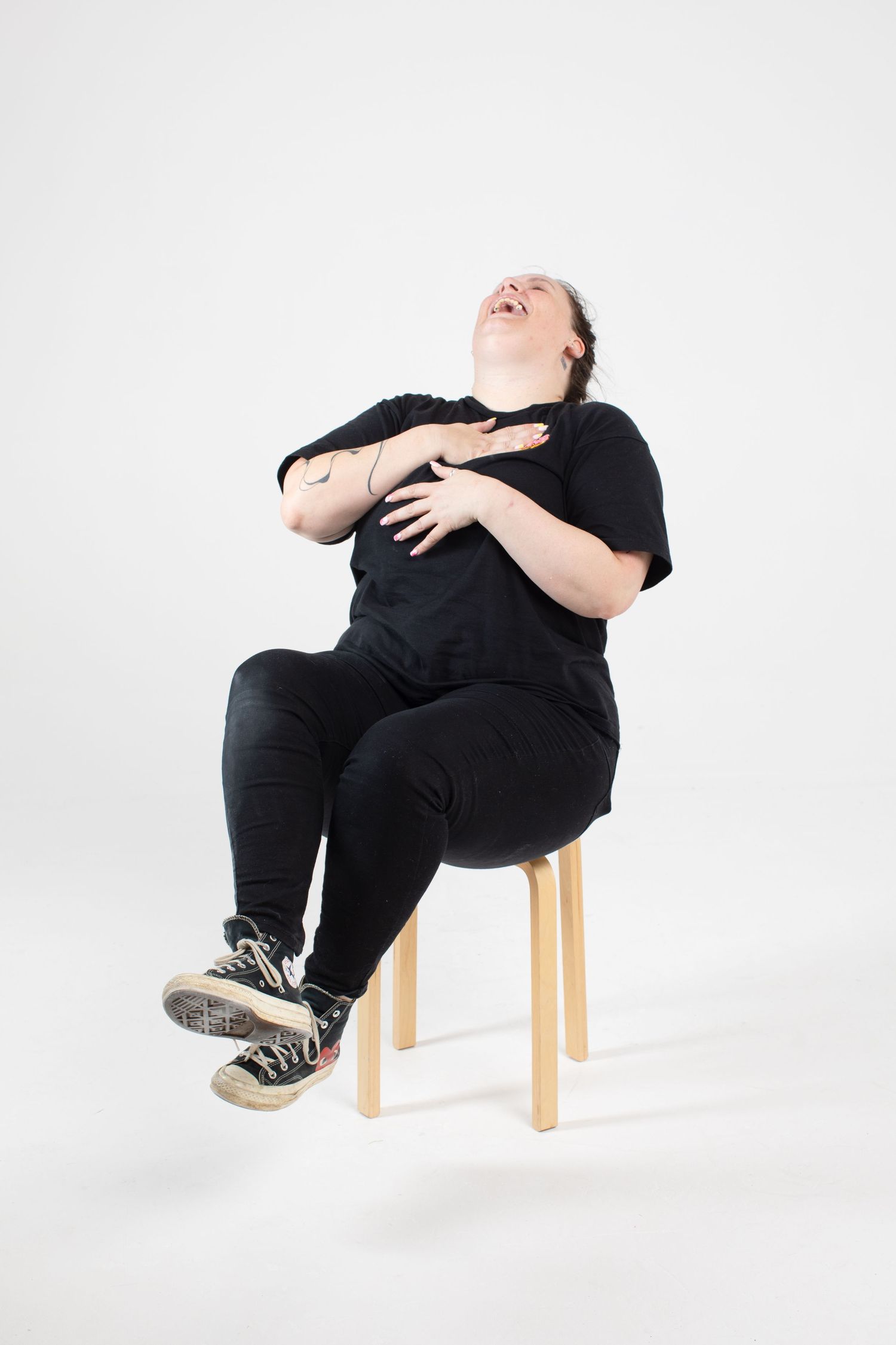 Person in black clothing sitting on wooden stool against white background in artistic poses.
