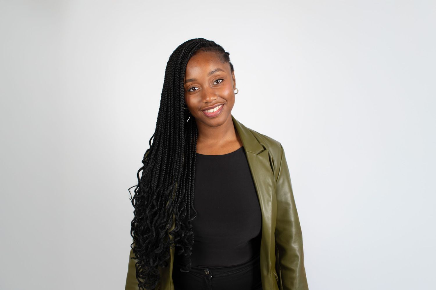Professional portrait of someone wearing a black top and olive green blazer against a white background.