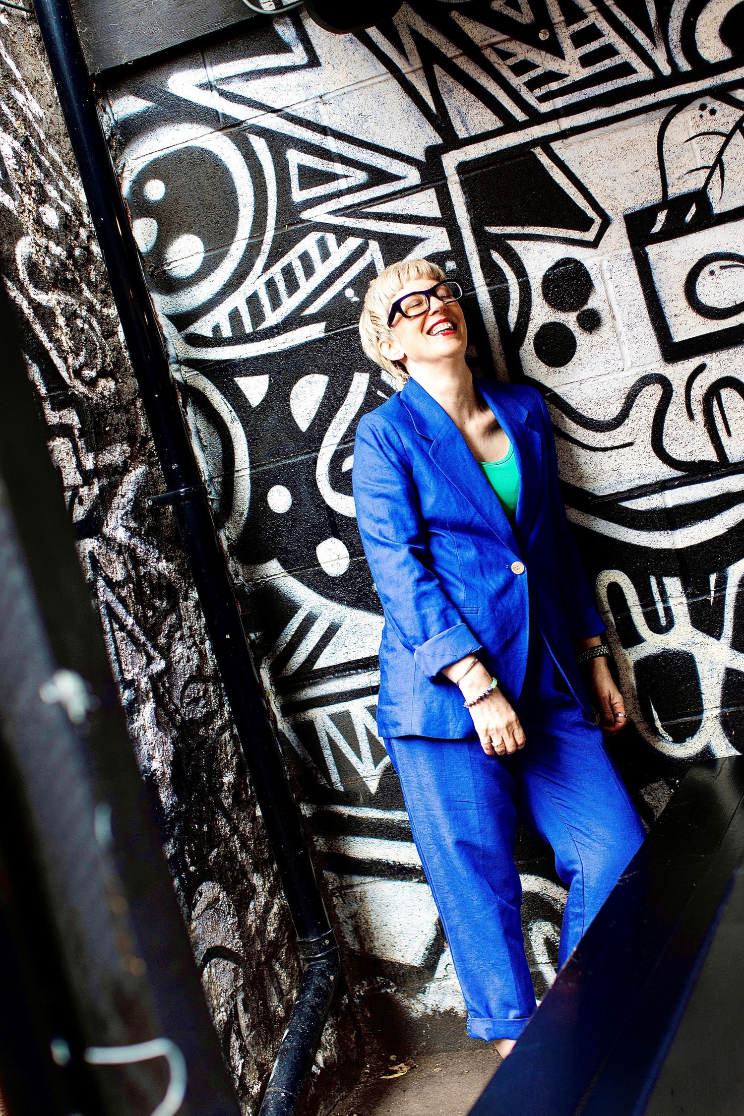 Woman in blue suit posing against graffiti wall with black and white street art.