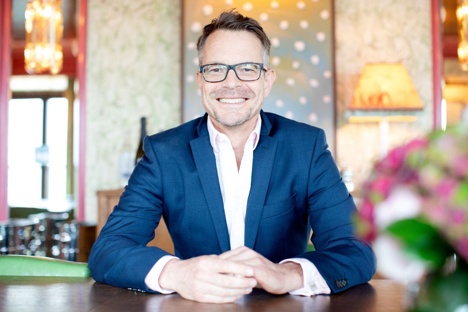 Professional business portrait in formal attire against warm interior background.