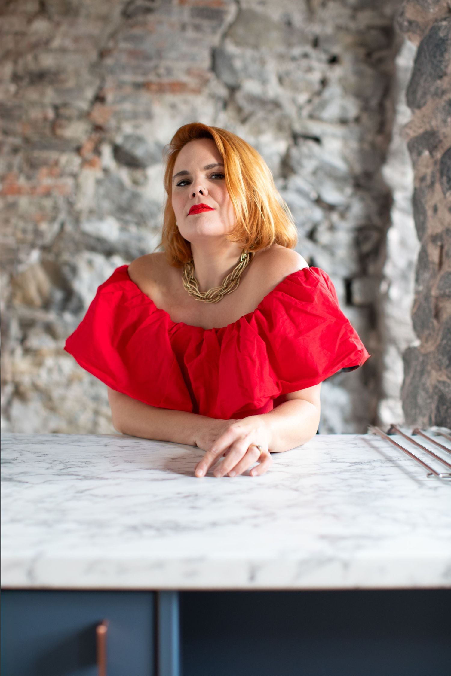 Artistic portrait series with red ruffled top against rustic brick wall and white surface.
