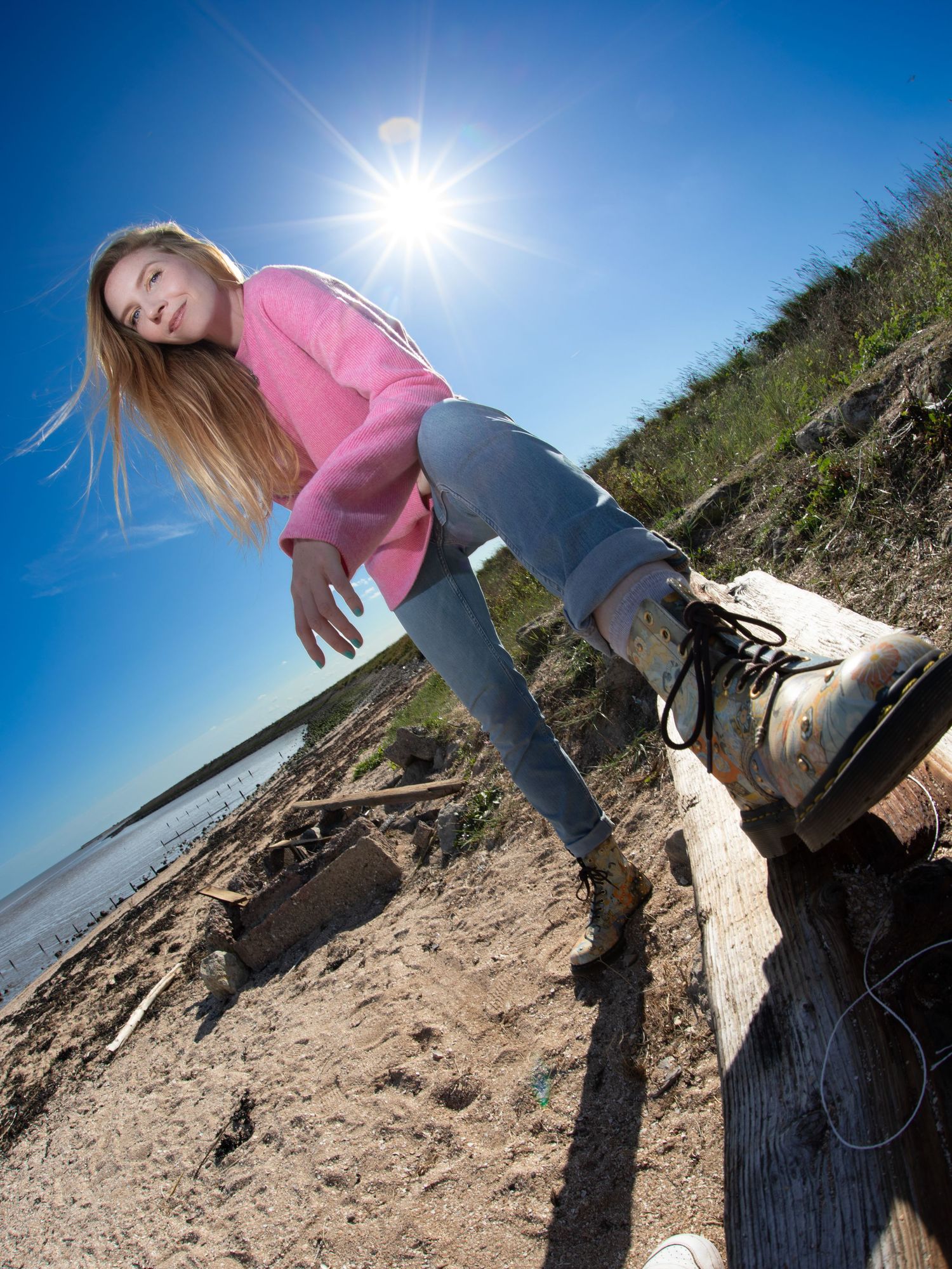 Dynamic beach photoshoot with pink top and jeans against bright blue sky and sandy backdrop.