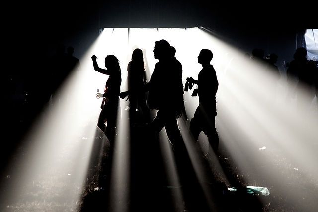 Silhouettes of four people standing in dramatic light beams inside a dark tunnel or warehouse.