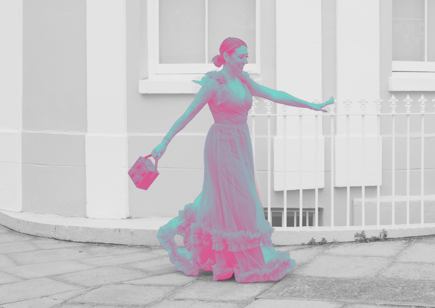 A woman in a colorful pink and teal flamenco dress poses gracefully outdoors, holding a small handbag.