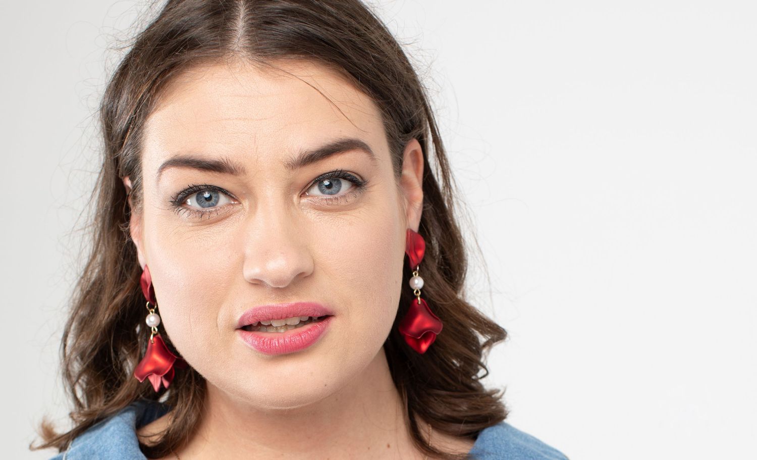 Portrait against white background wearing blue top and red statement earrings.