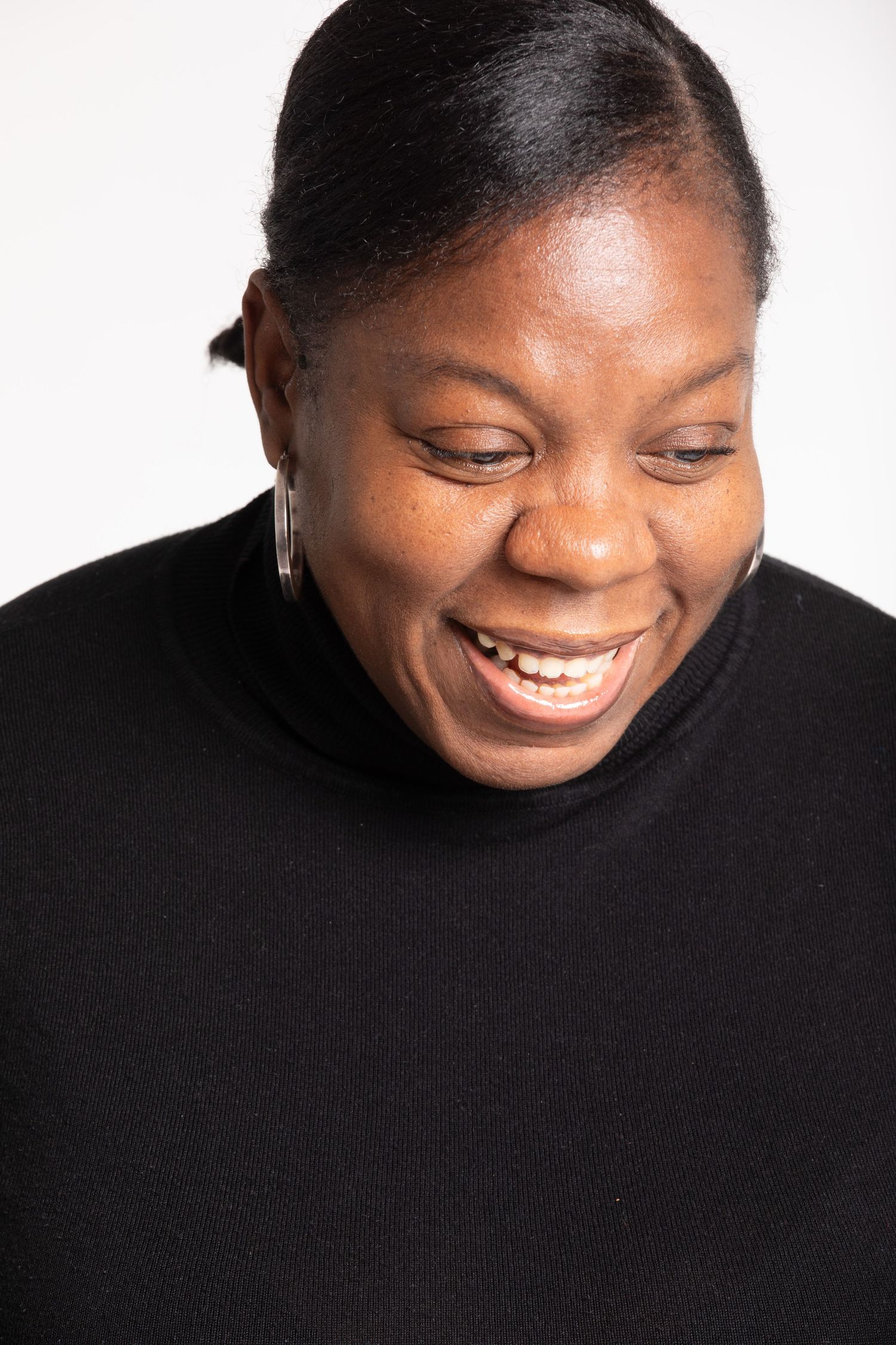 Joyful Black woman in black turtleneck laughing with eyes closed against white background.