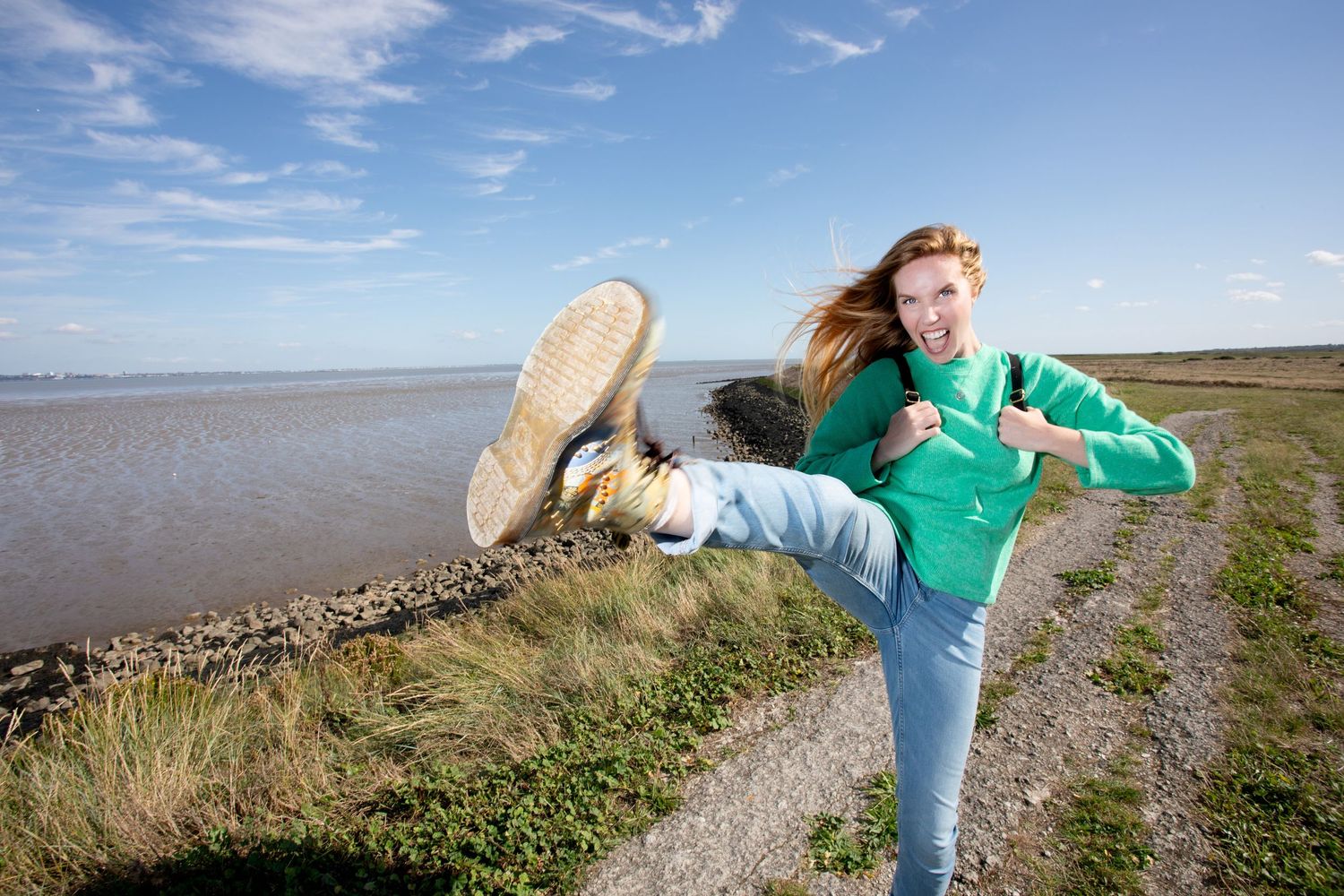 Outdoor photoshoot on coastal path with green sweater and playful poses against blue sky.