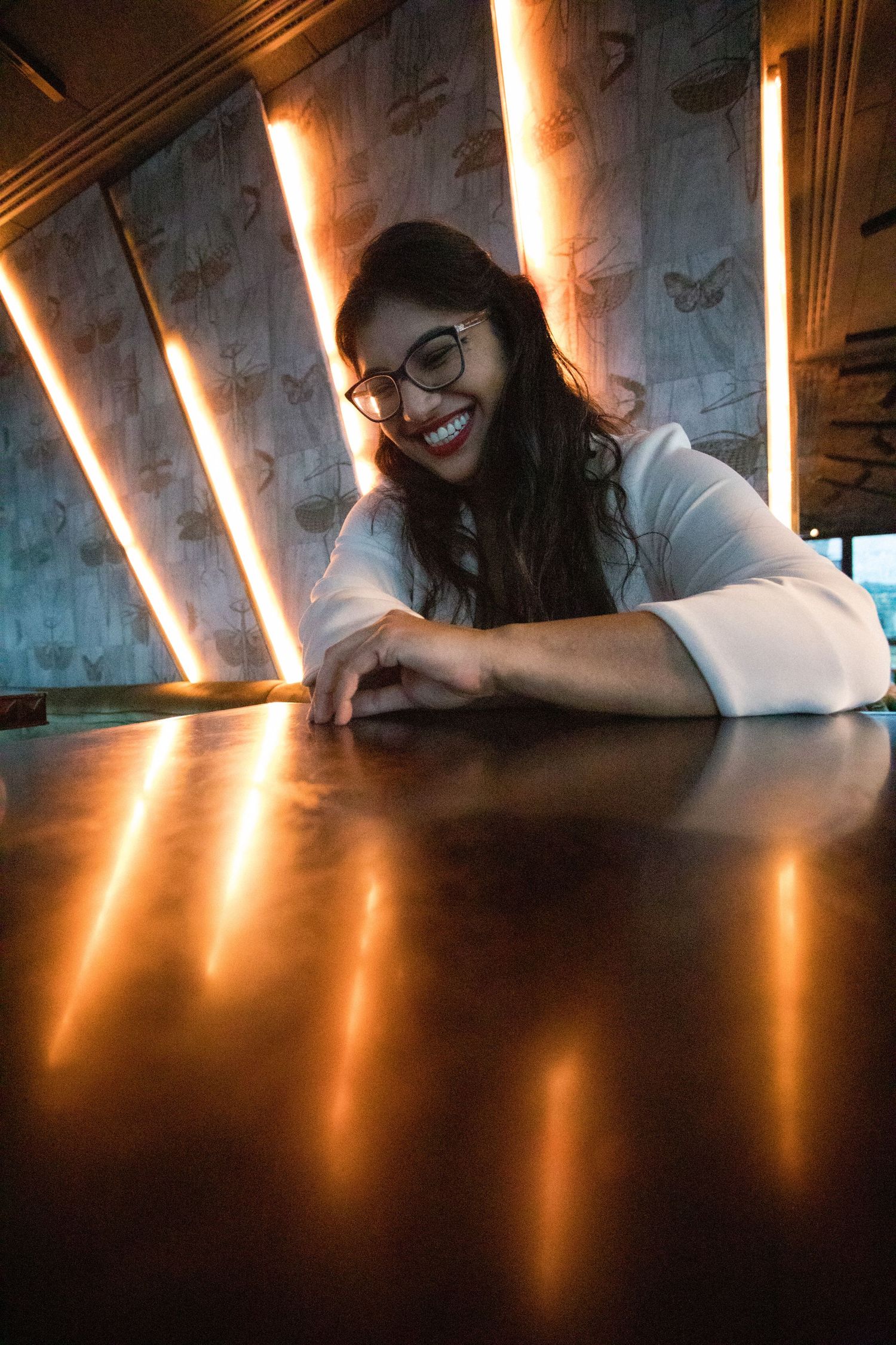 Artistic portrait with dramatic lighting showing someone smiling at a table with illuminated wall patterns.