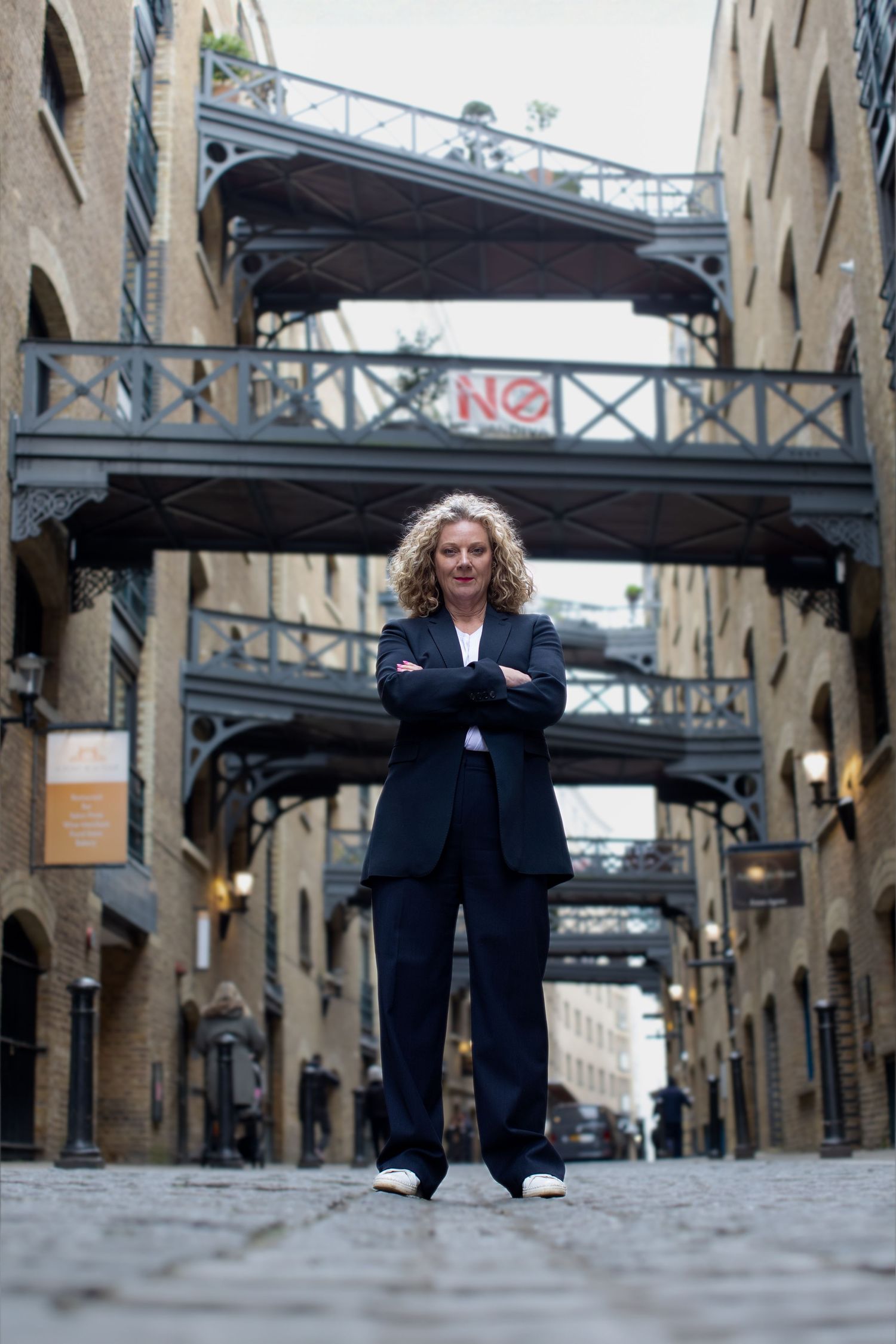 Urban fashion photography along historic brick warehouses with industrial bridges overhead.