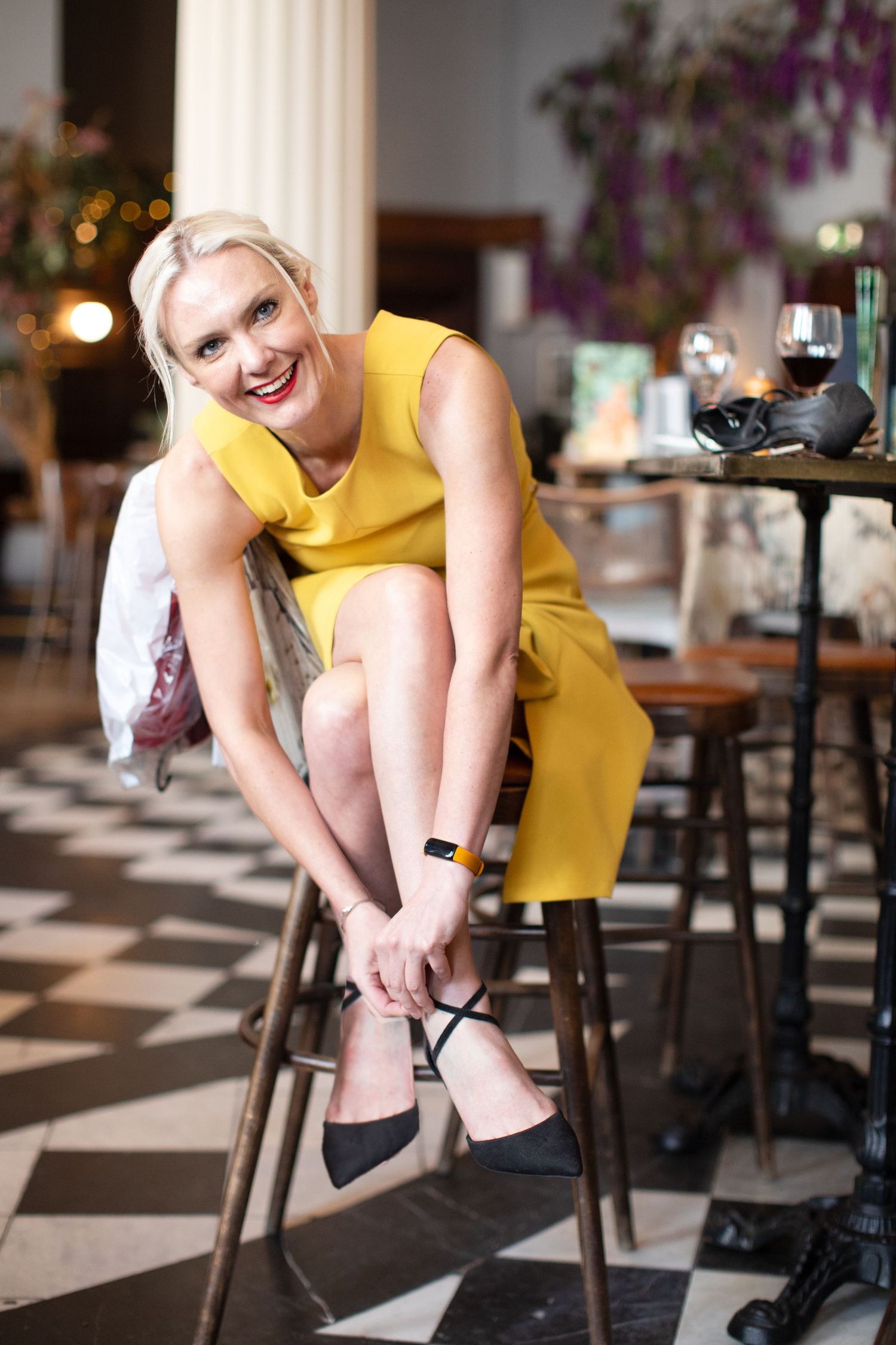 Person in yellow dress sitting on bar stool adjusting footwear in restaurant setting.
