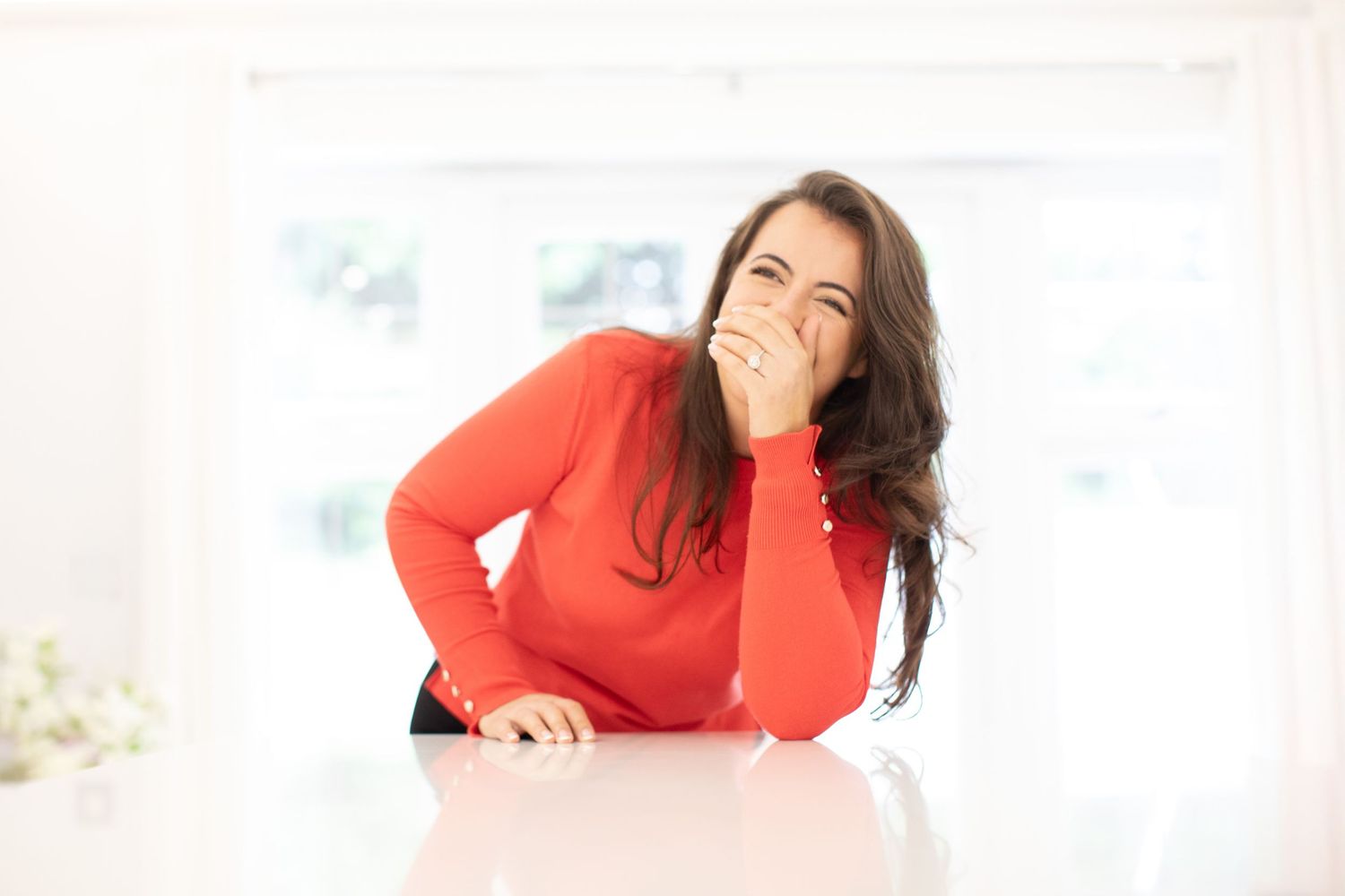 Person in red sweater lounging and laughing against bright interior background.