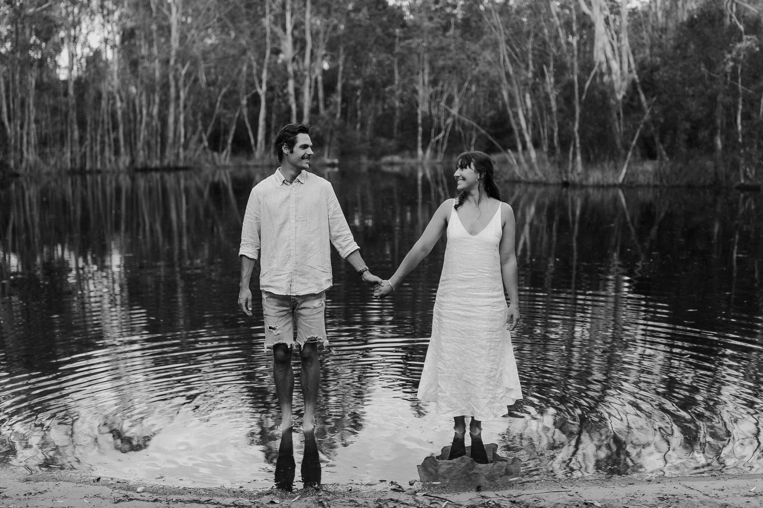 Black and white wedding photos showing couples in romantic poses by a lake surrounded by trees.