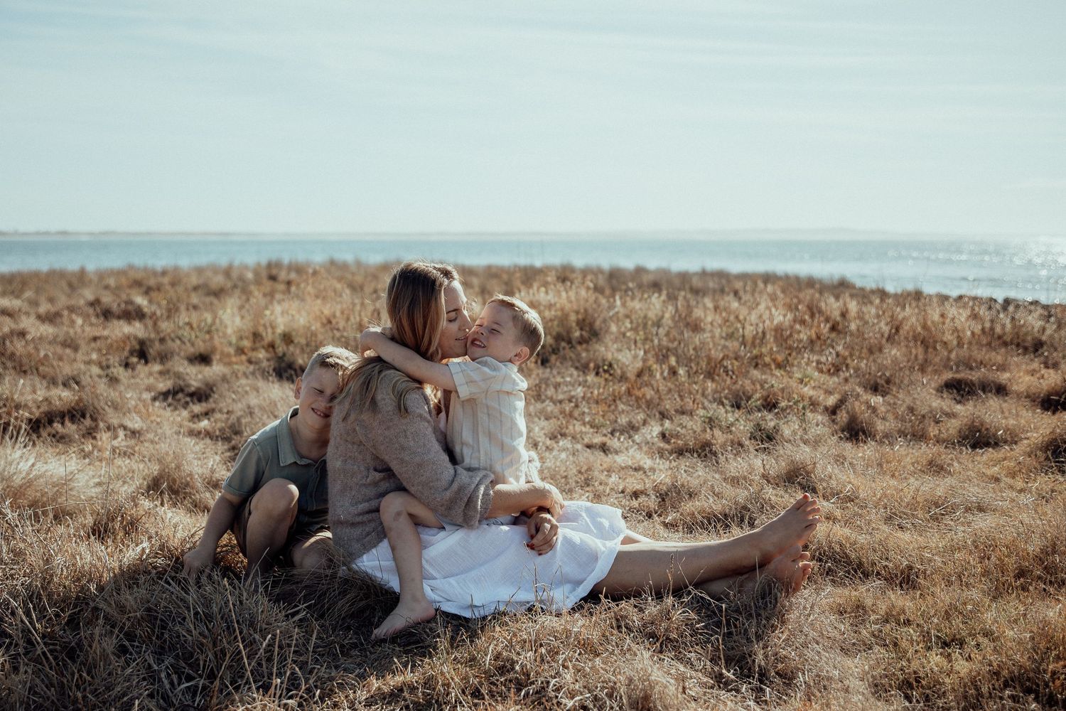 A romantic couple sits together on grassy coastal cliffs overlooking the ocean.