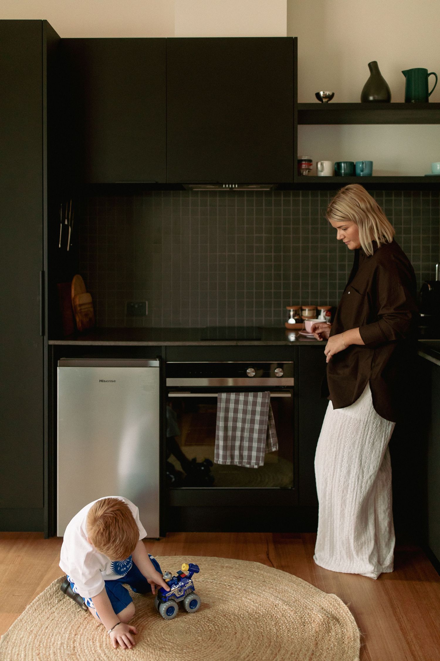 Modern kitchen interior with black tiles and wooden floors while a child plays.