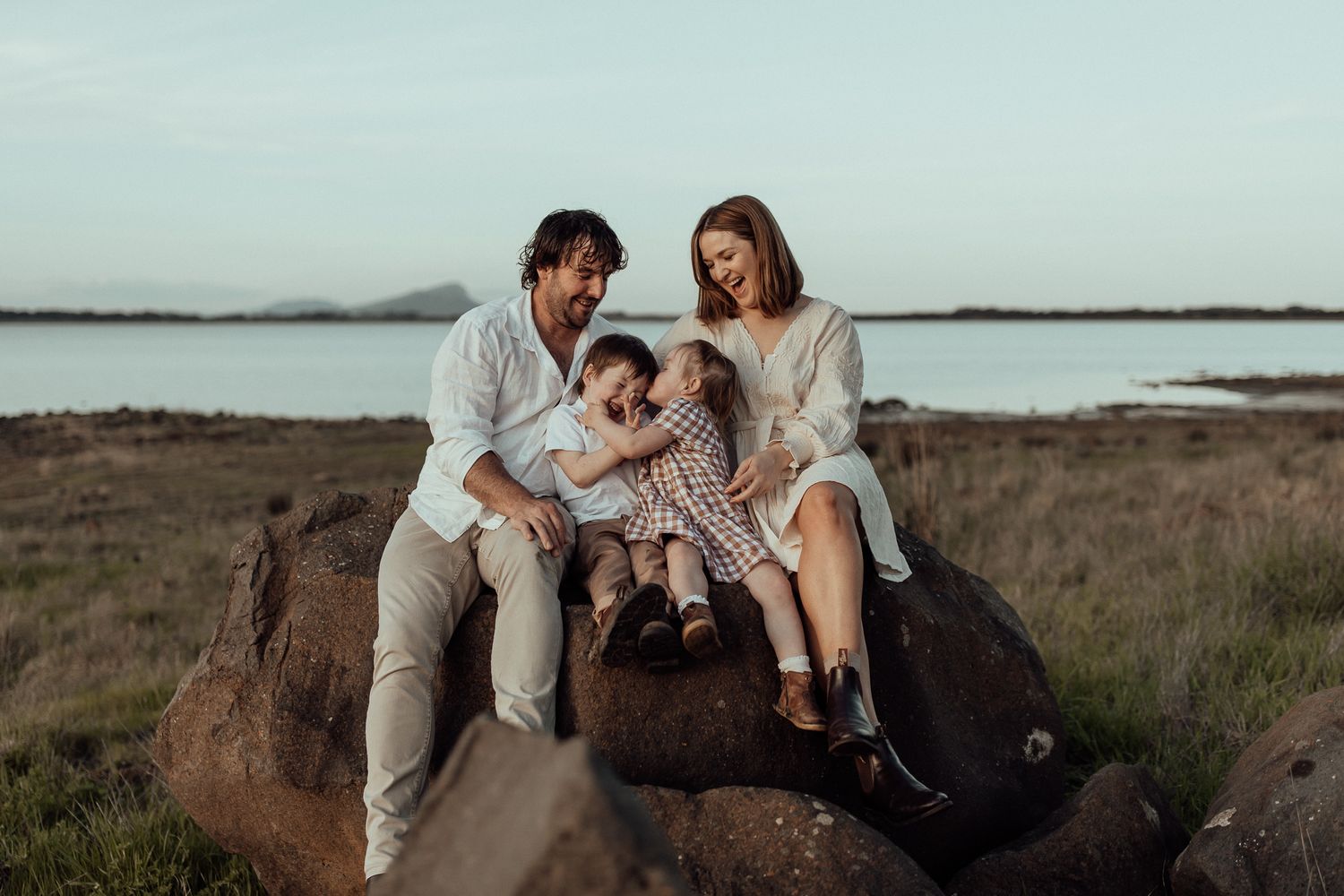 Family sitting together on coastal rocks during golden hour photography session.