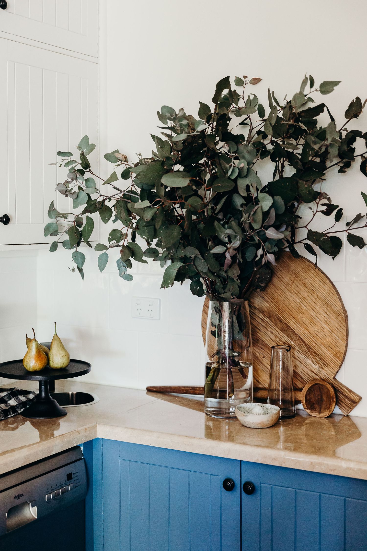 Modern kitchen counter with blue cabinets decorated with eucalyptus branches and wooden cutting boards.