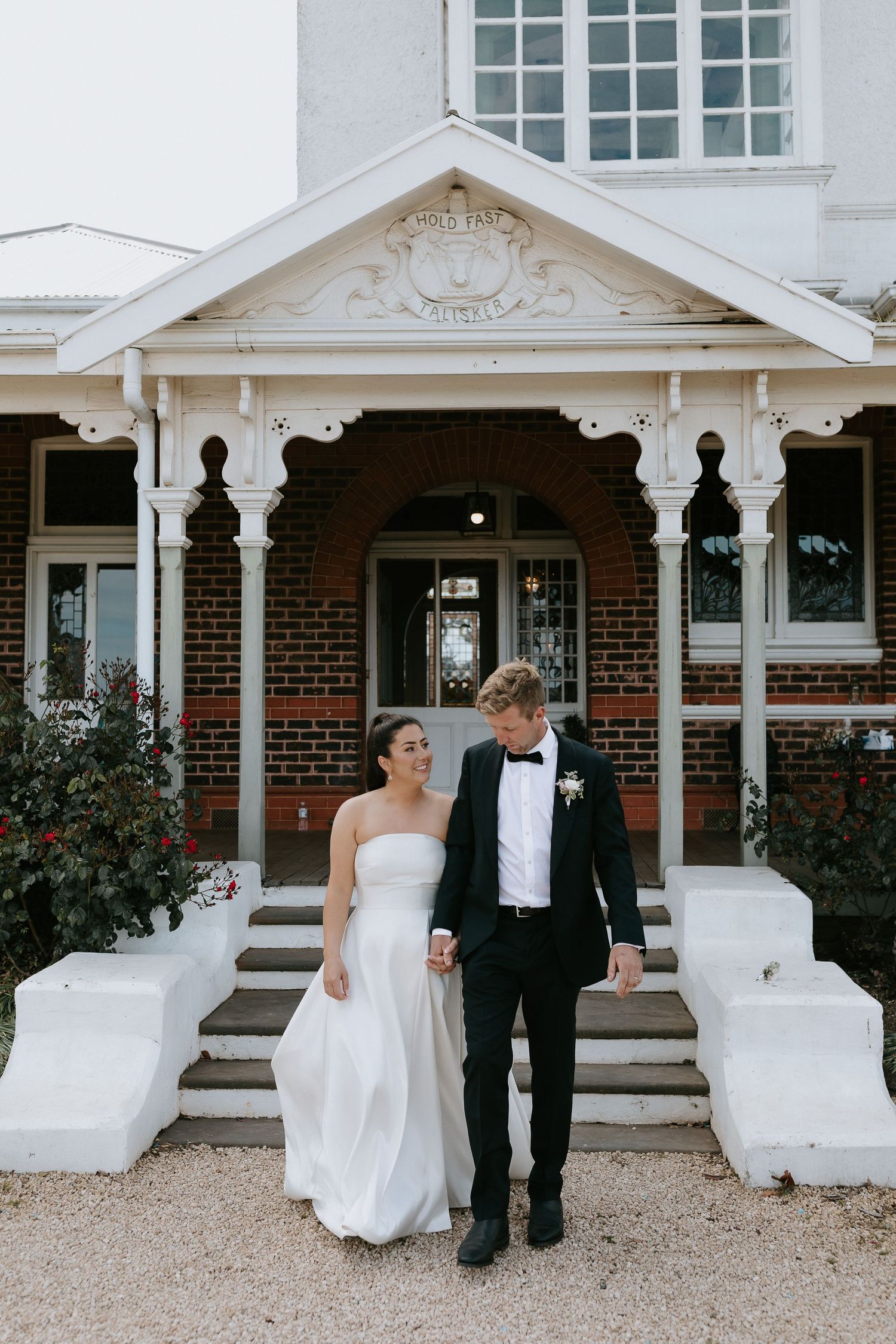 Elegant white colonial-style entrance with ornate pillars and decorative pediment. Bride and groom framed in front of it.