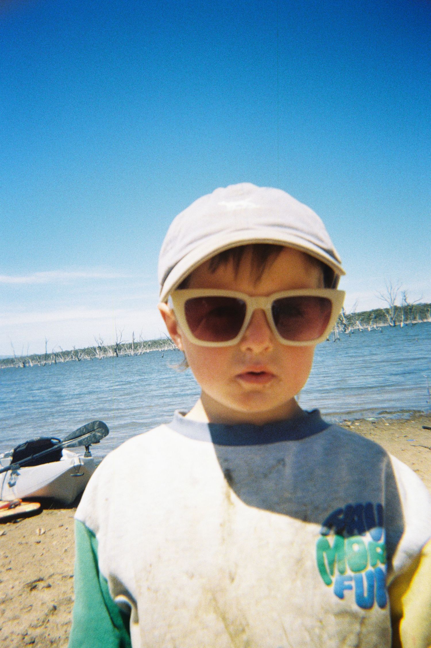 Beachside portrait with sunglasses and baseball cap against blue water backdrop.