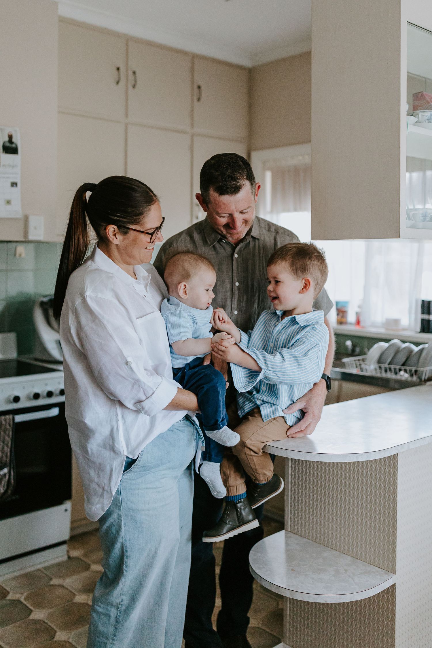A family shares tender moments in their bright kitchen, interacting around a white counter.