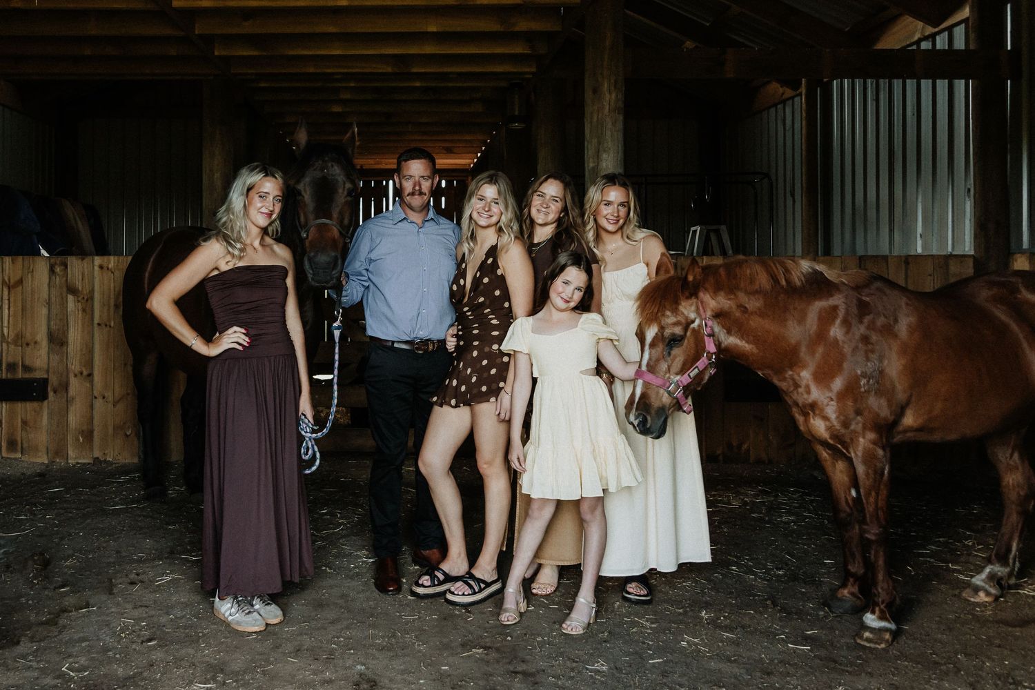 Family gathering in dimly lit rustic barn interior with horse.