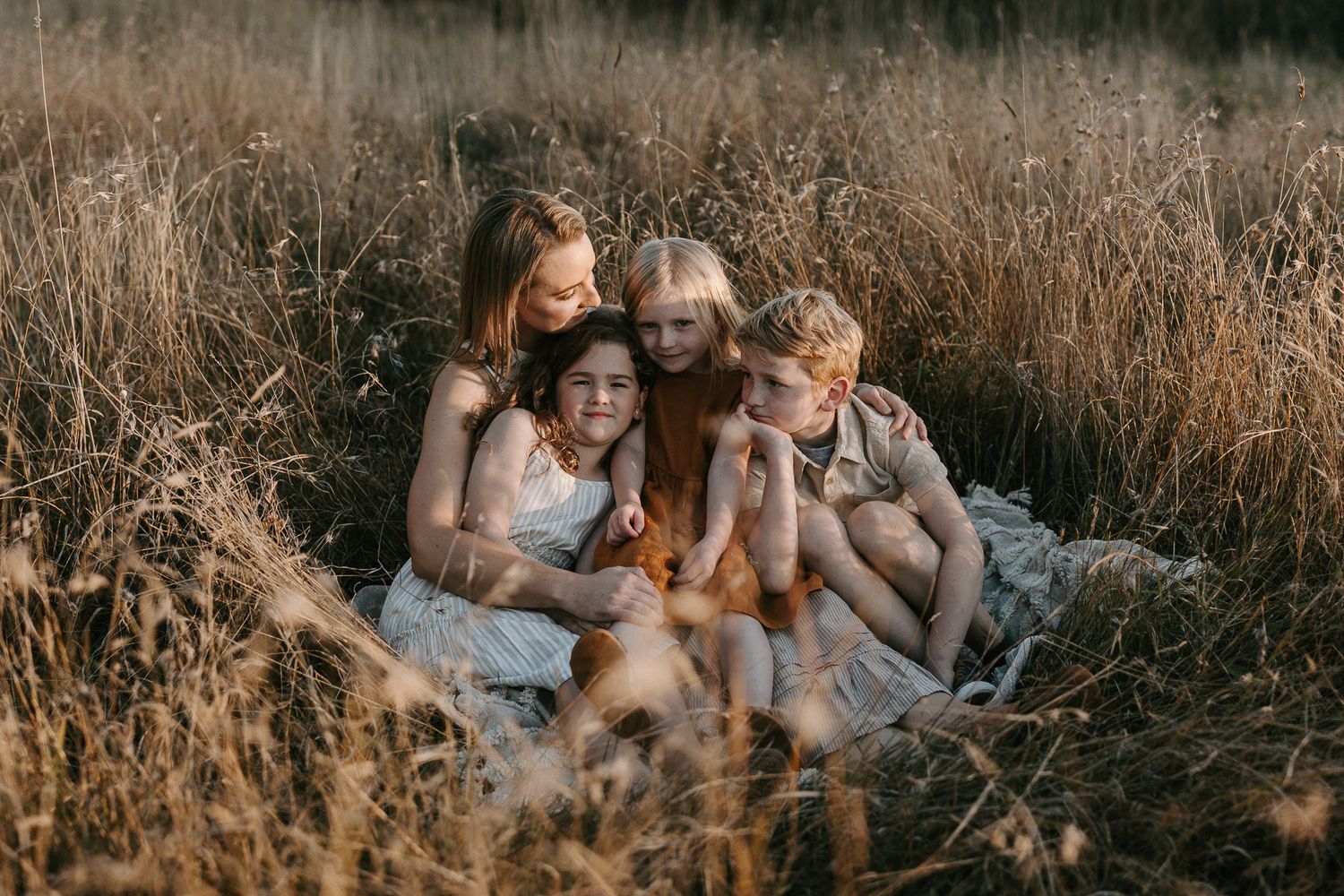 Family group relaxing in tall grass field during sunset photoshoot.