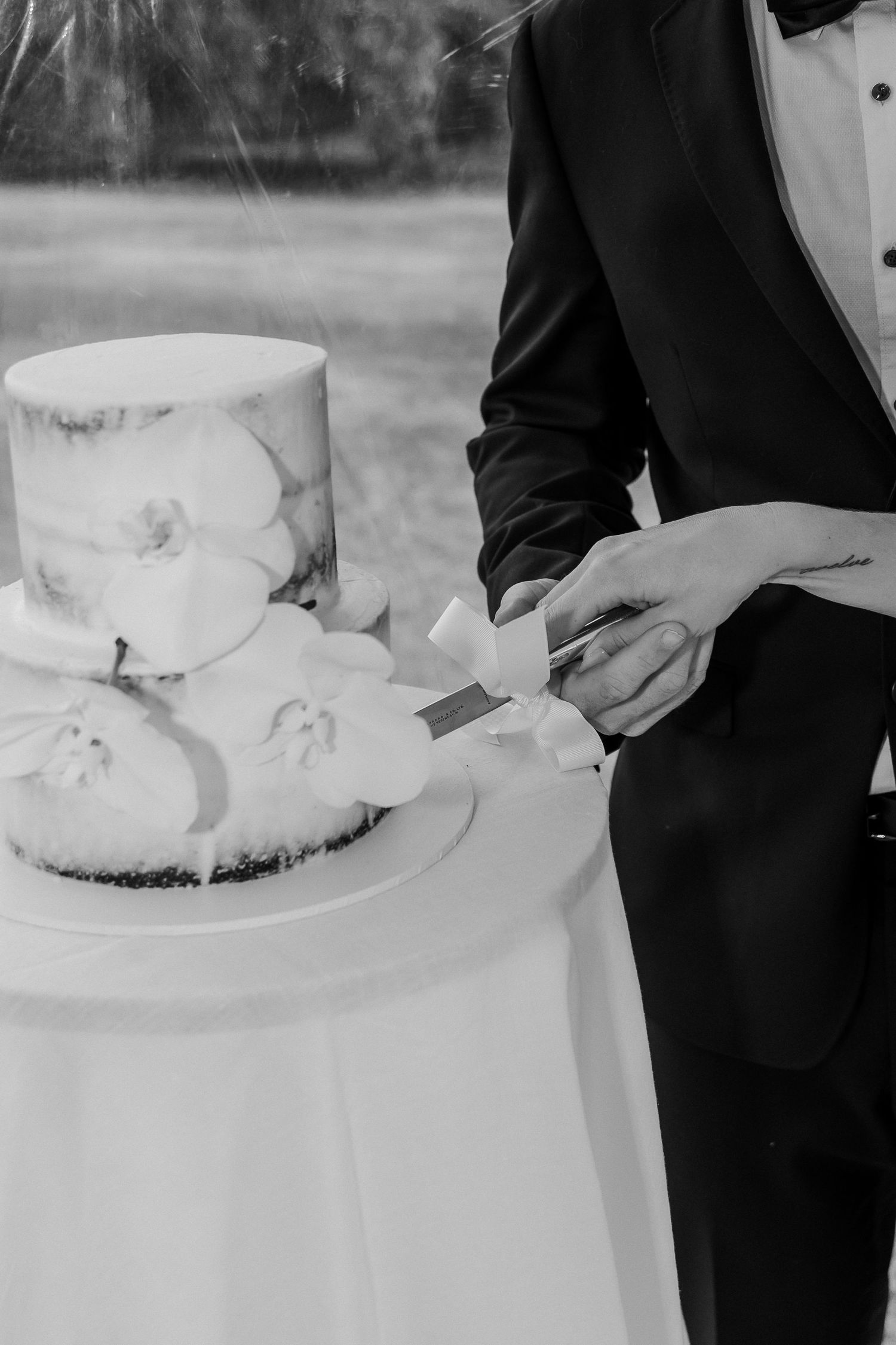 Wedding cake being cut on a white tablecloth with formal attire visible.